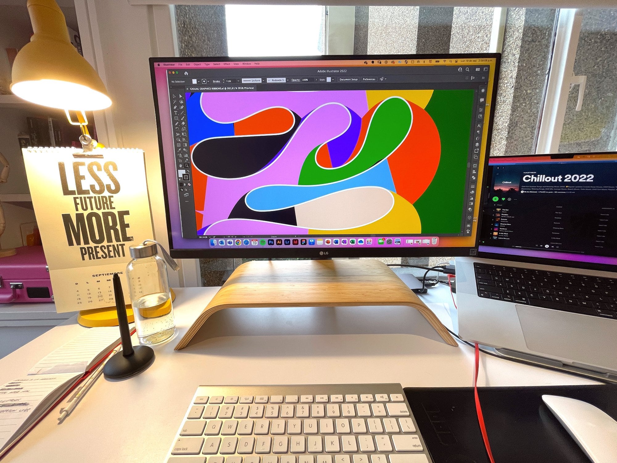 A vibrant desk setup with a yellow lamp and a “Less future, more present” calendar
