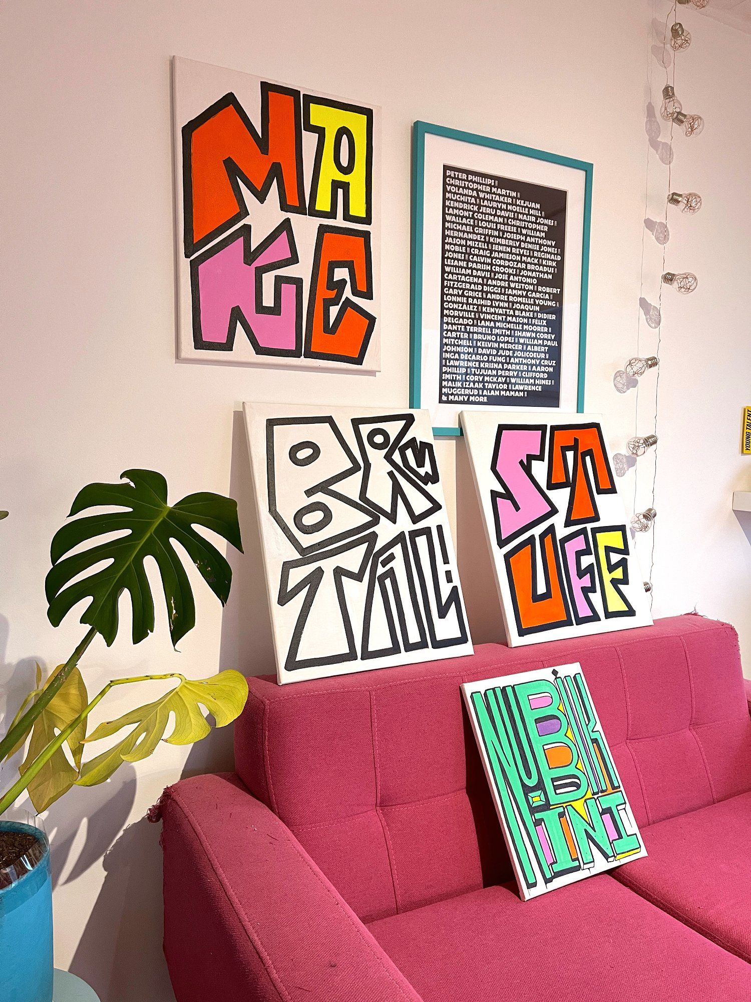 A pink sofa with lots of typography prints and monstera plant