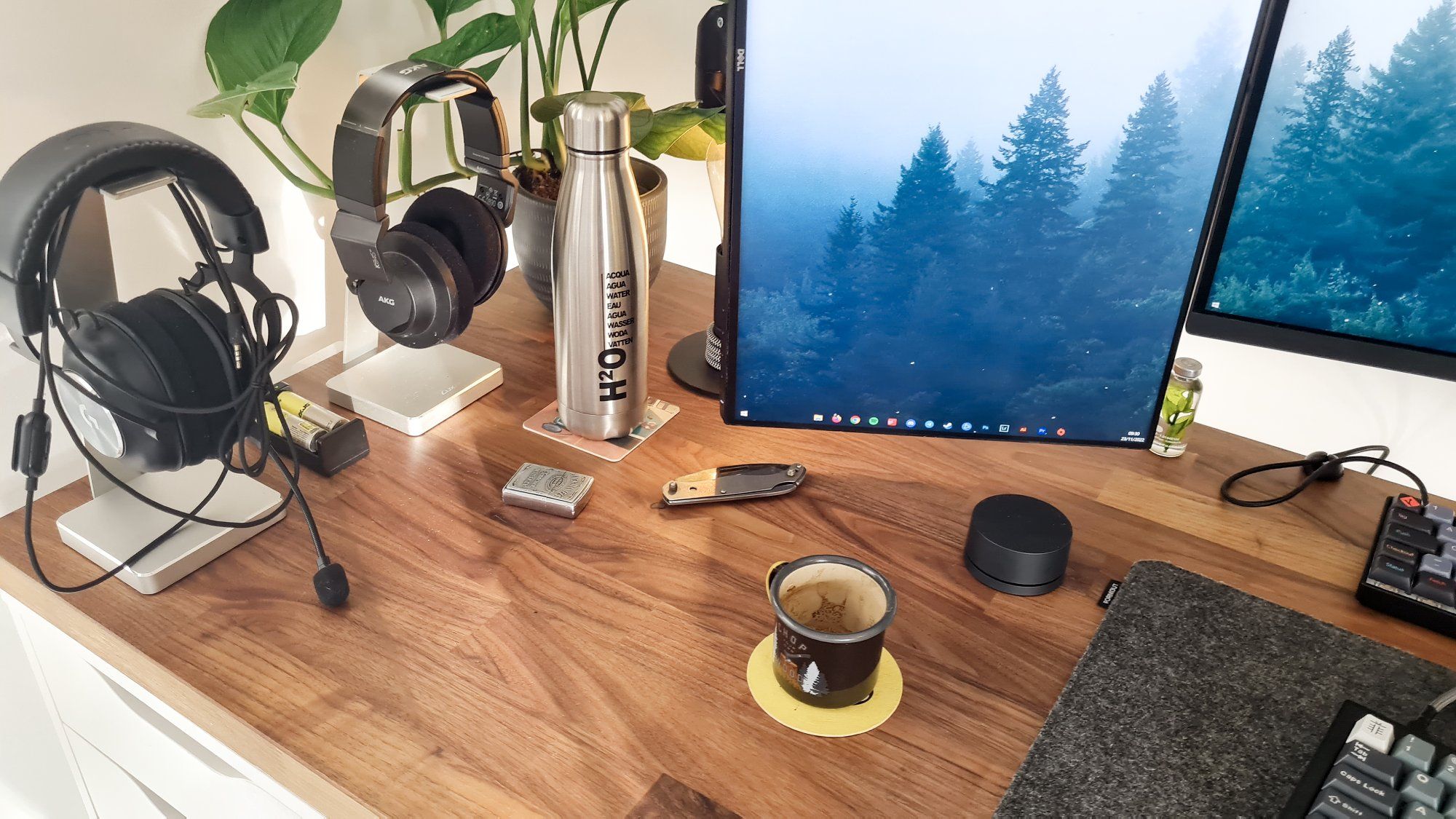 A home office desk setup with a pair of headphones, coffee mug, water bottle, one vertical, and one horizontal monitor