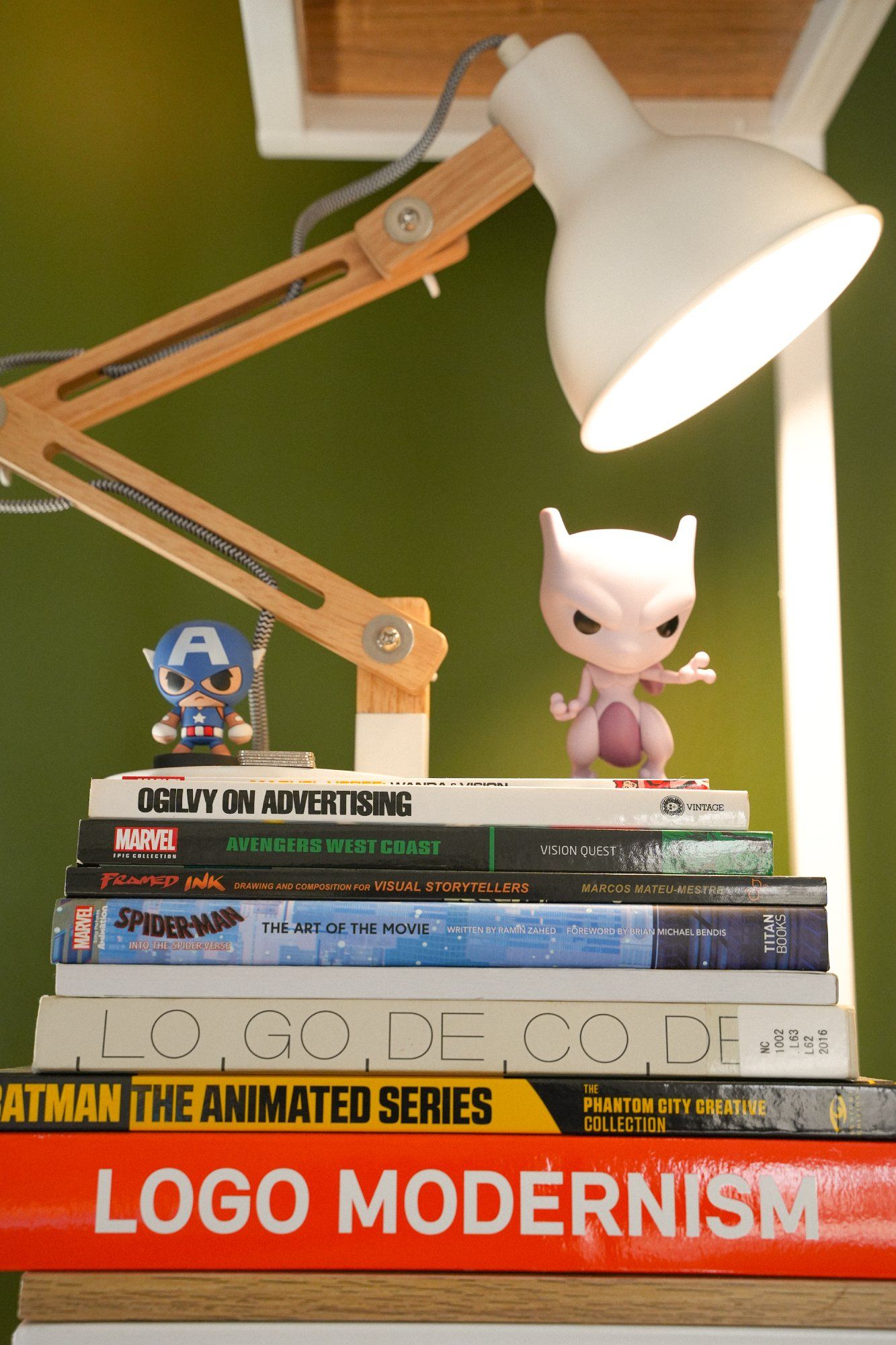 A stack of books on design, illustration and advertising, with two figurines and a lamp placed on top