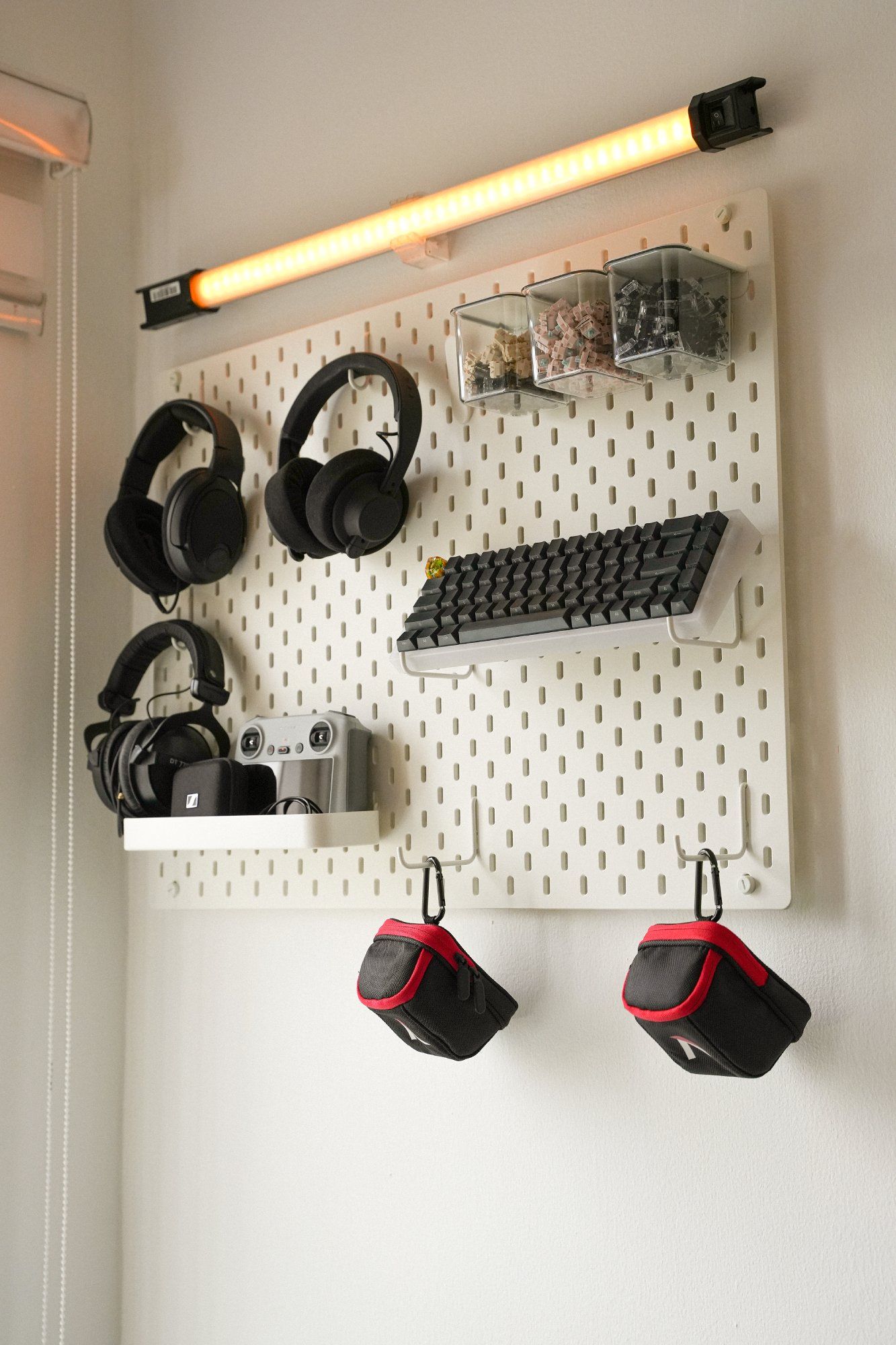 A pegboard displaying home office accessories and peripherals such as headphones, keyboard keycaps, and other items