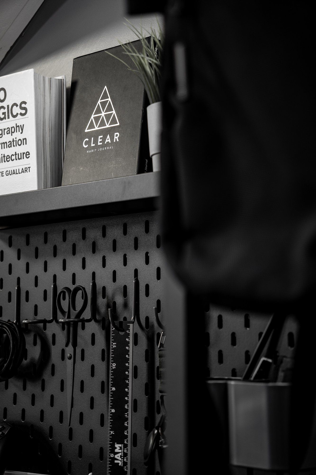 The home office essentials, such as scissors, pens, and rulers hanging on a black metal pegboard