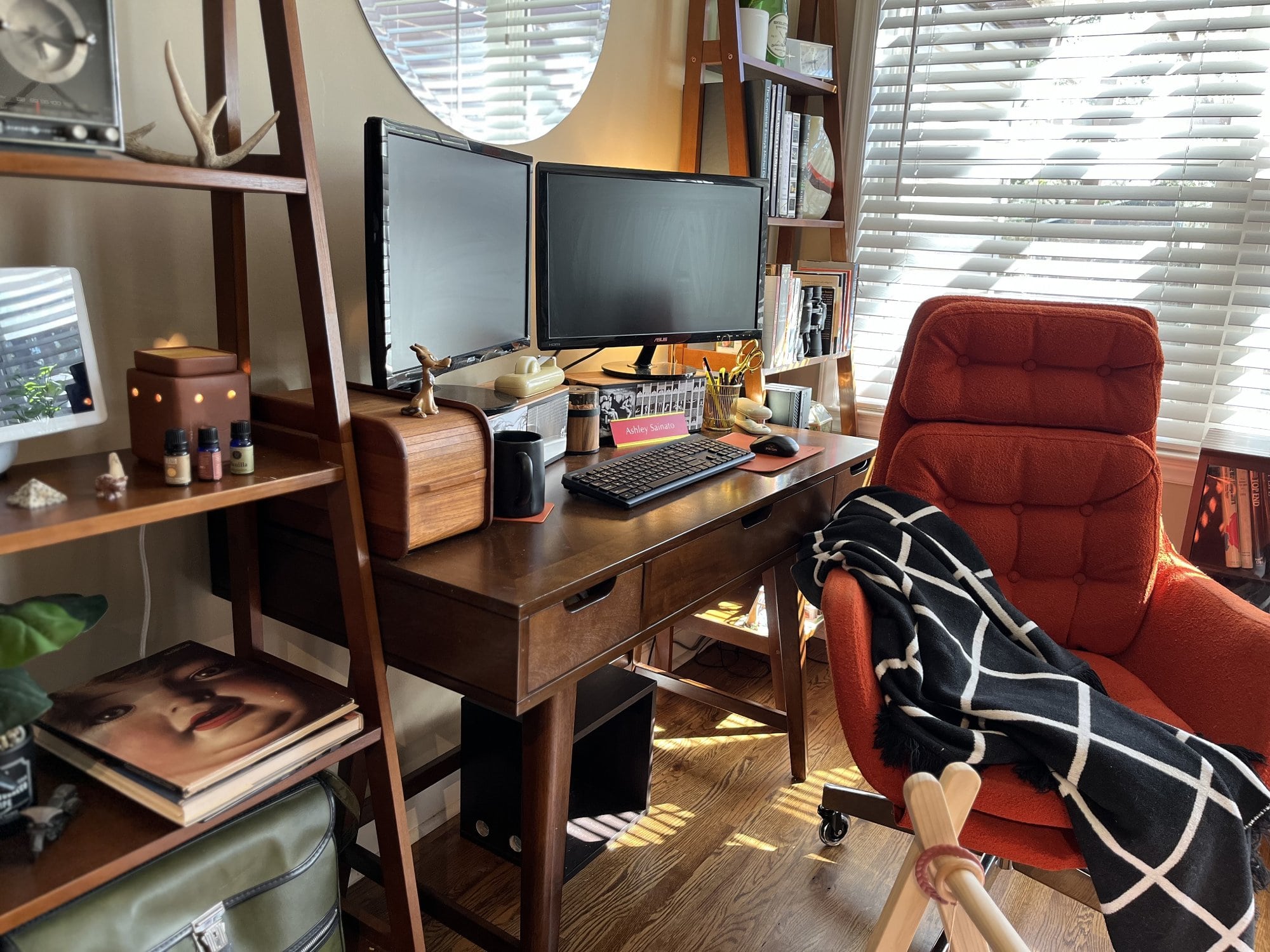 A side view of an organised and bright workspace featuring the wooden desk with a dual-monitor setup and a cosy mid-century armchair