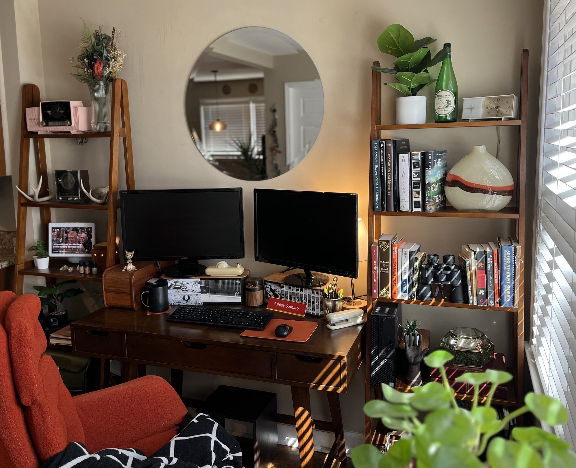 A spacious and airy two-monitor workspace featuring the round mirror and tall bookshelves