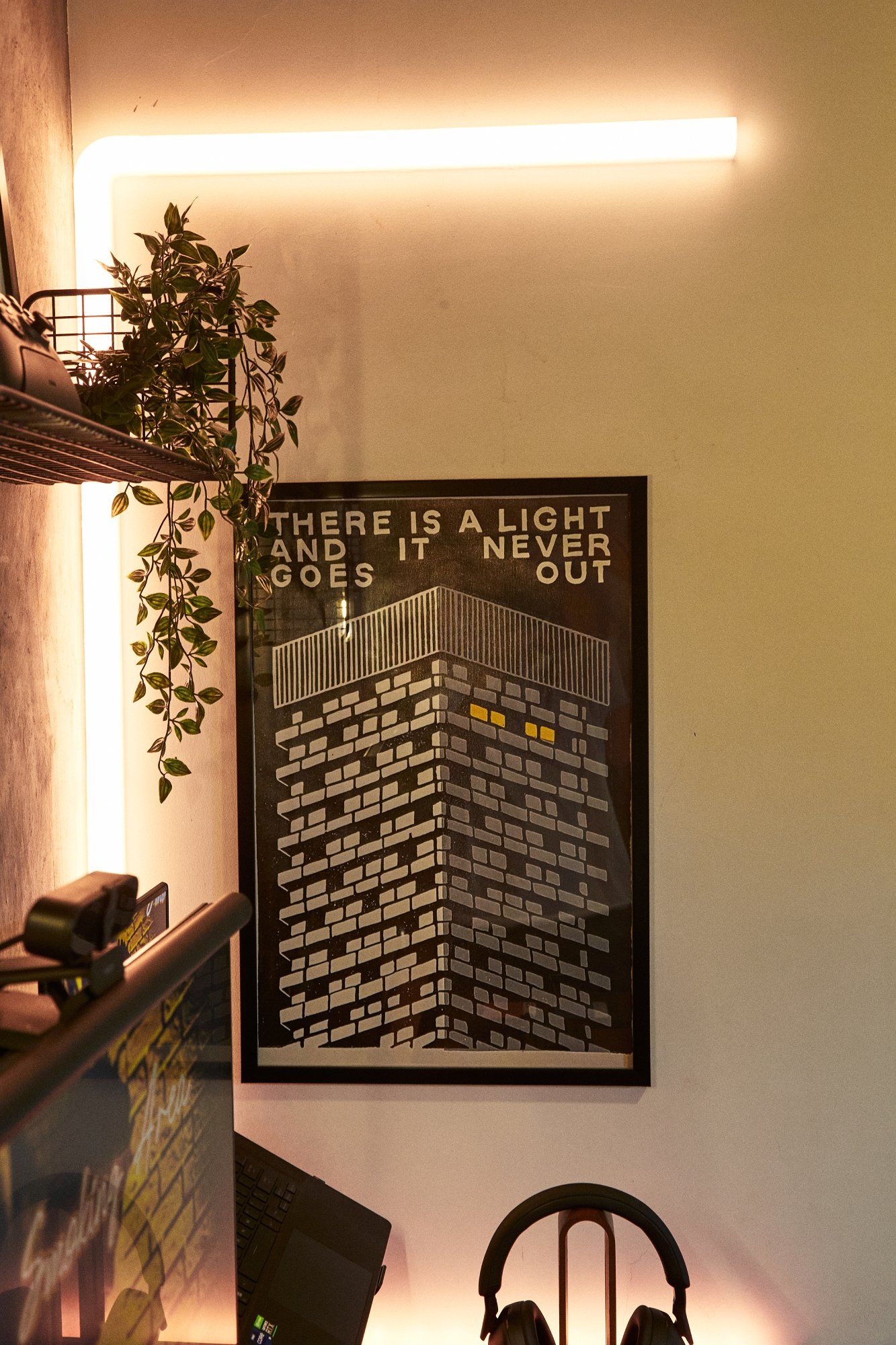 A dark home office desk setup with a “There is a light and it never goes out” poster on the wall