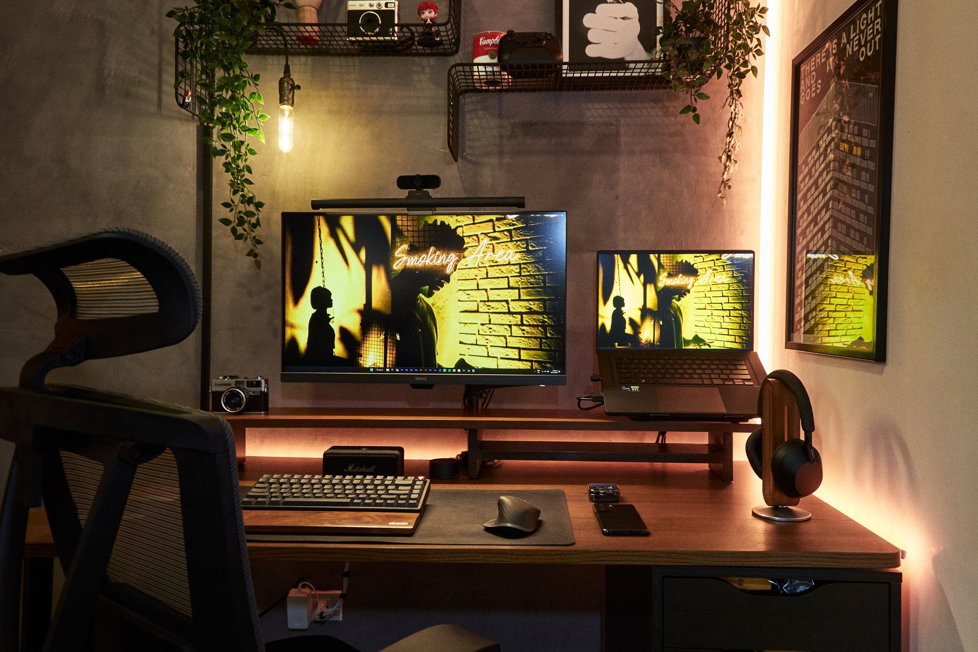 A dark desk setup with a monitor and a laptop, both displaying the Smoking Area desktop wallpaper