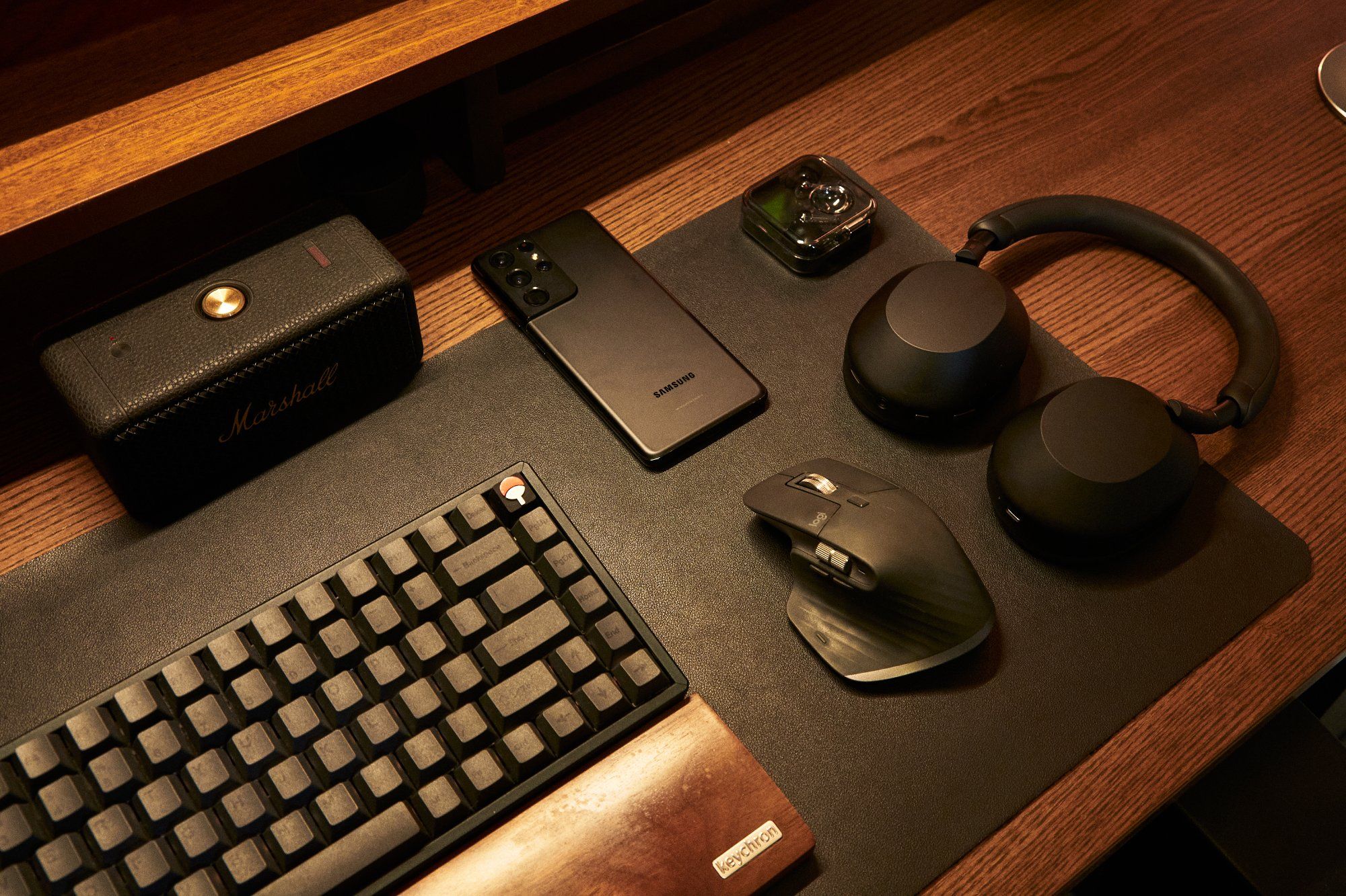 A Keychron K2 keyboard, Logitech MX Master3 mouse, Marshall speaker, Sony headphones, and Samsung smartphone on the home office desk