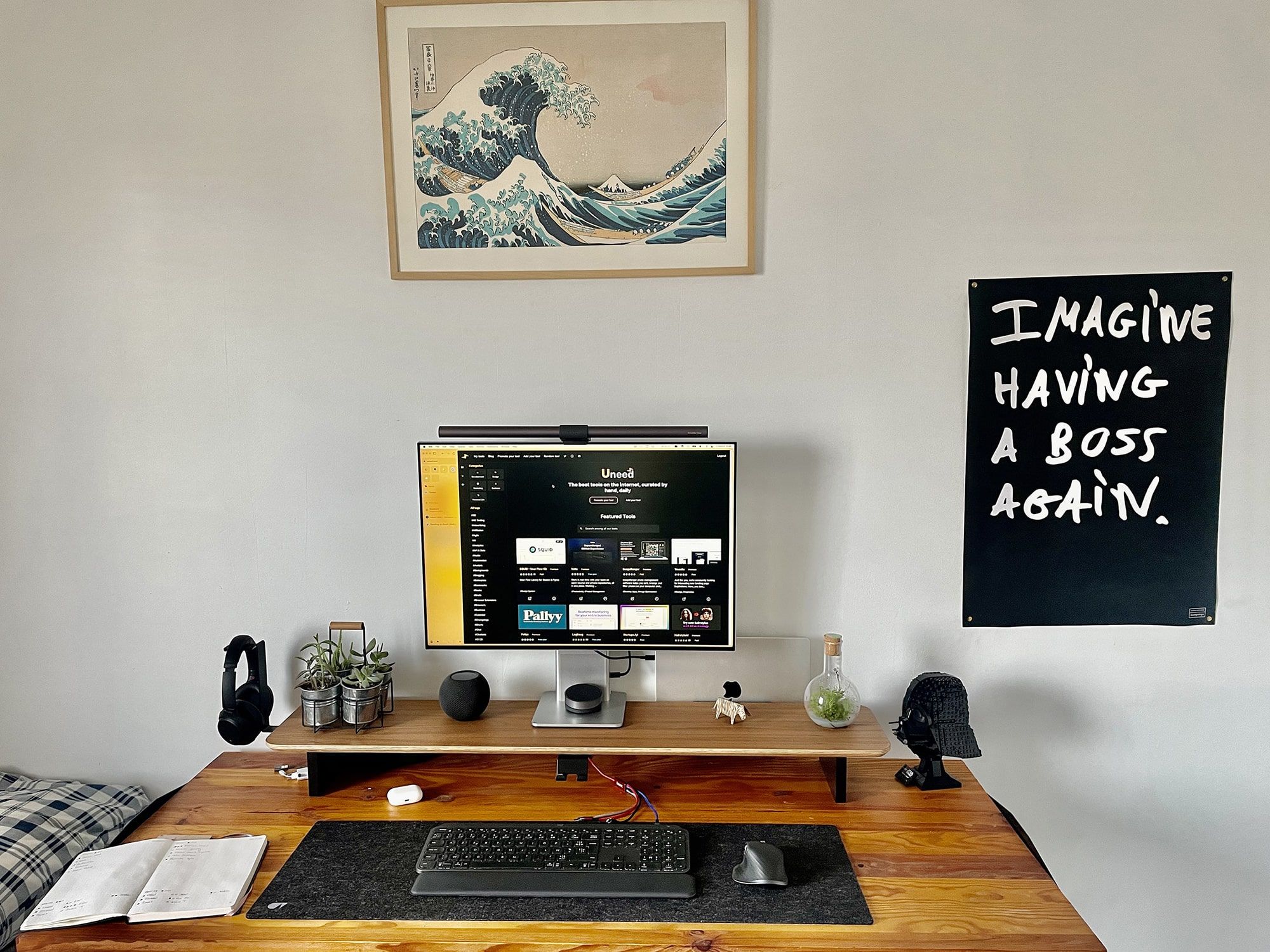 A black framed poster on the right side of a modern workspace, featuring white bold text that reads “Imagine having a boss again” against a dark background