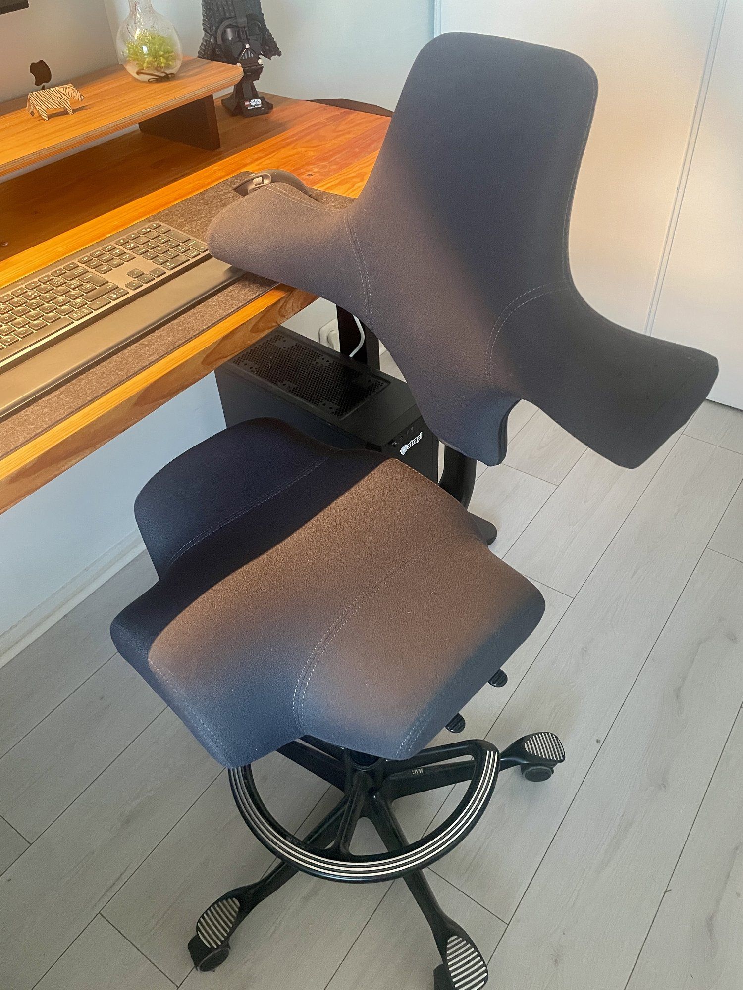 A close-up of an ergonomic HAG Capisco chair in a modern workspace, showcasing its adjustable features and sleek design. The chair comes with a 265mm lift height (overall chair height is 51.5″; seat height is 22.5-33″), which is handy to use with a standing desk