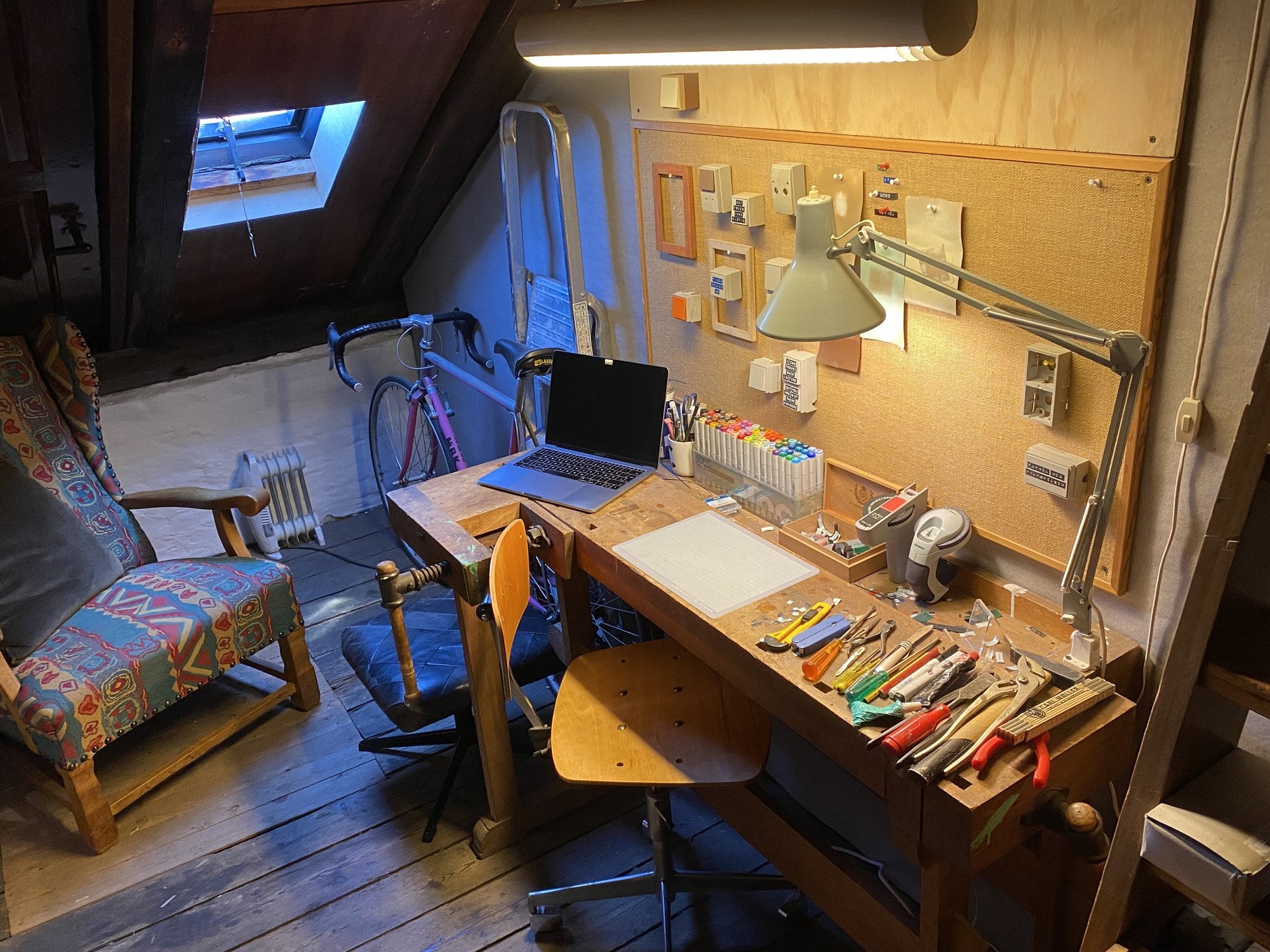 An artistic attic workspace featuring a wooden carpenters bench desk from 1980s and a cosy vintage chair