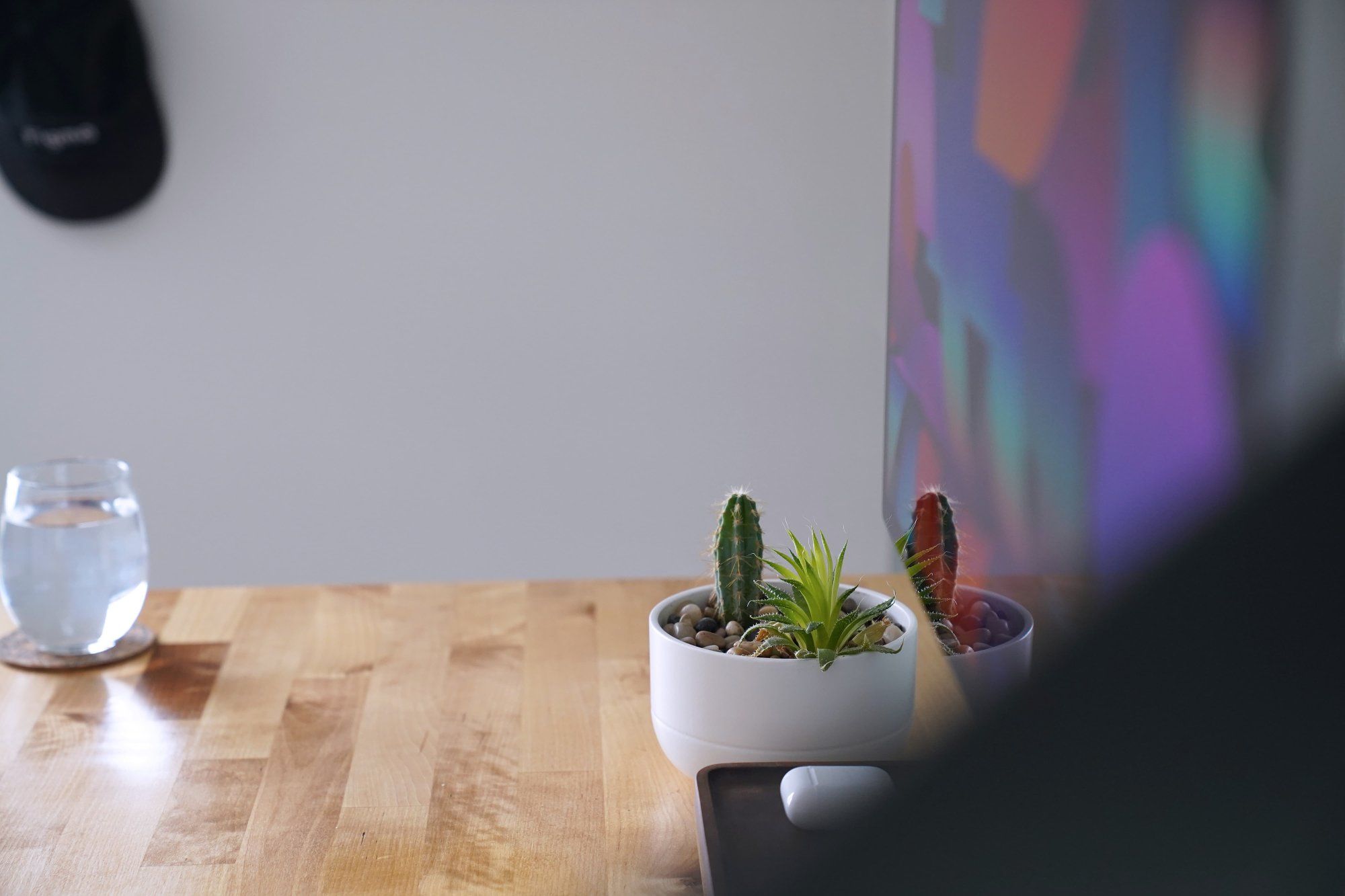 A side view of a minimalist desk setup, which shows a cactus and succulent planter, along with a clear water glass and a monitor