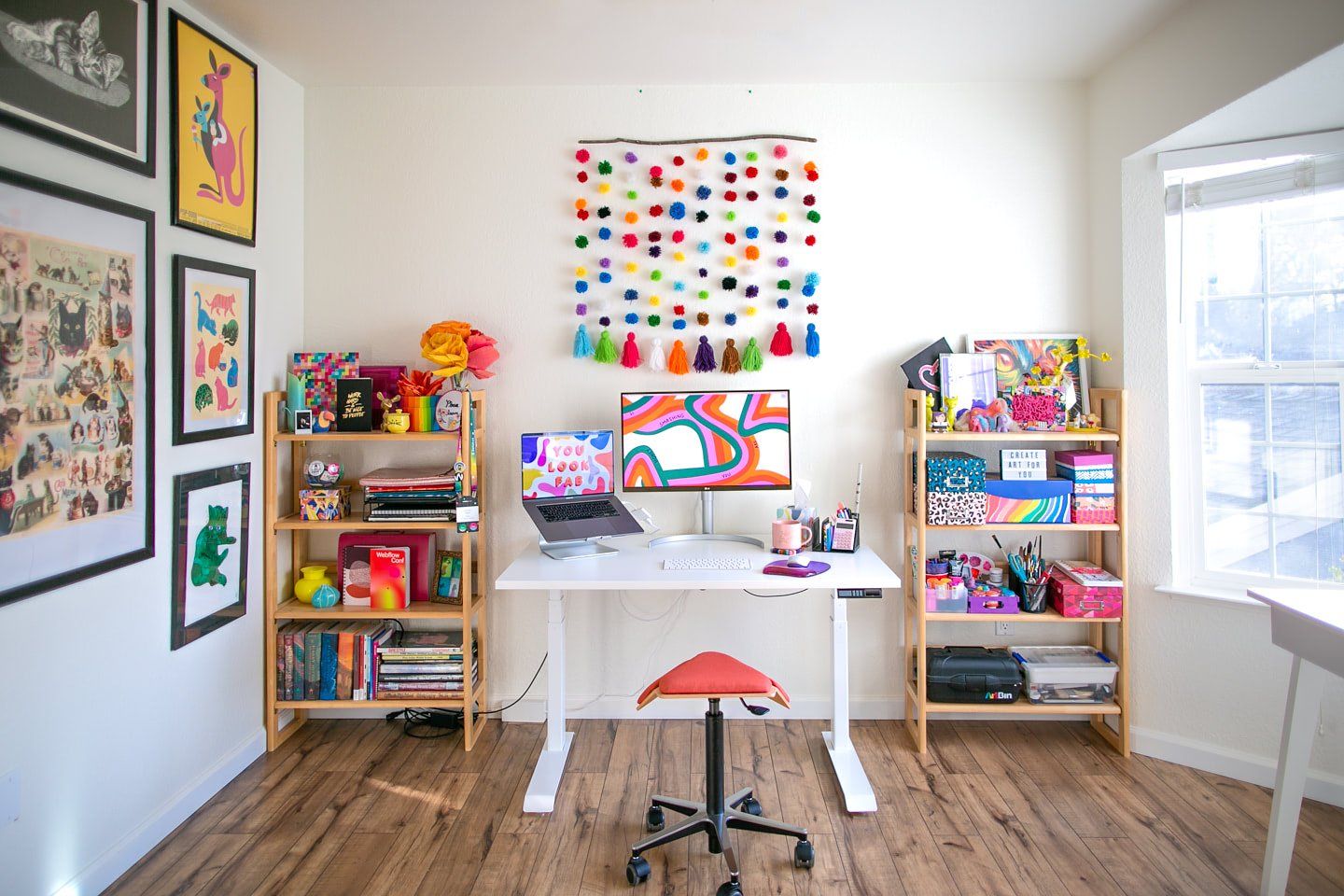 A vibrant home office with a standing desk, an Iloa saddle chair, plus a large number of personal items and colourful artwork