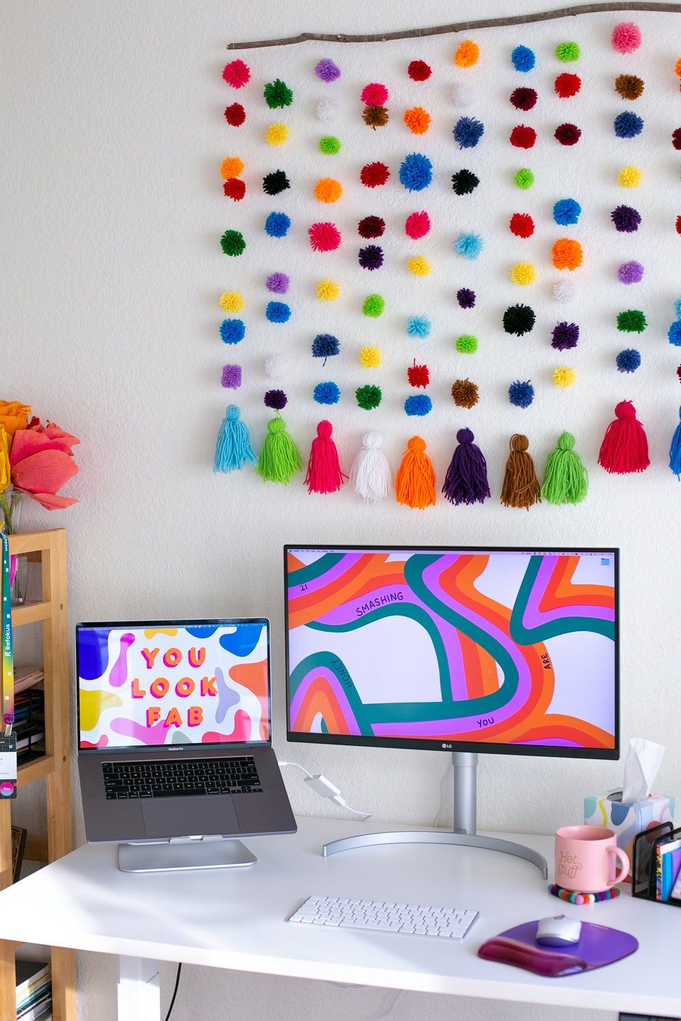 A bright home desk setup with a pom pom tassel garland hanging on the wall