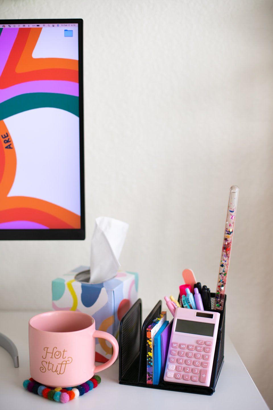 A little pink calculator, colourful stationery, and a ‘Hot Stuff’ mug rest on a felted coaster on the desk