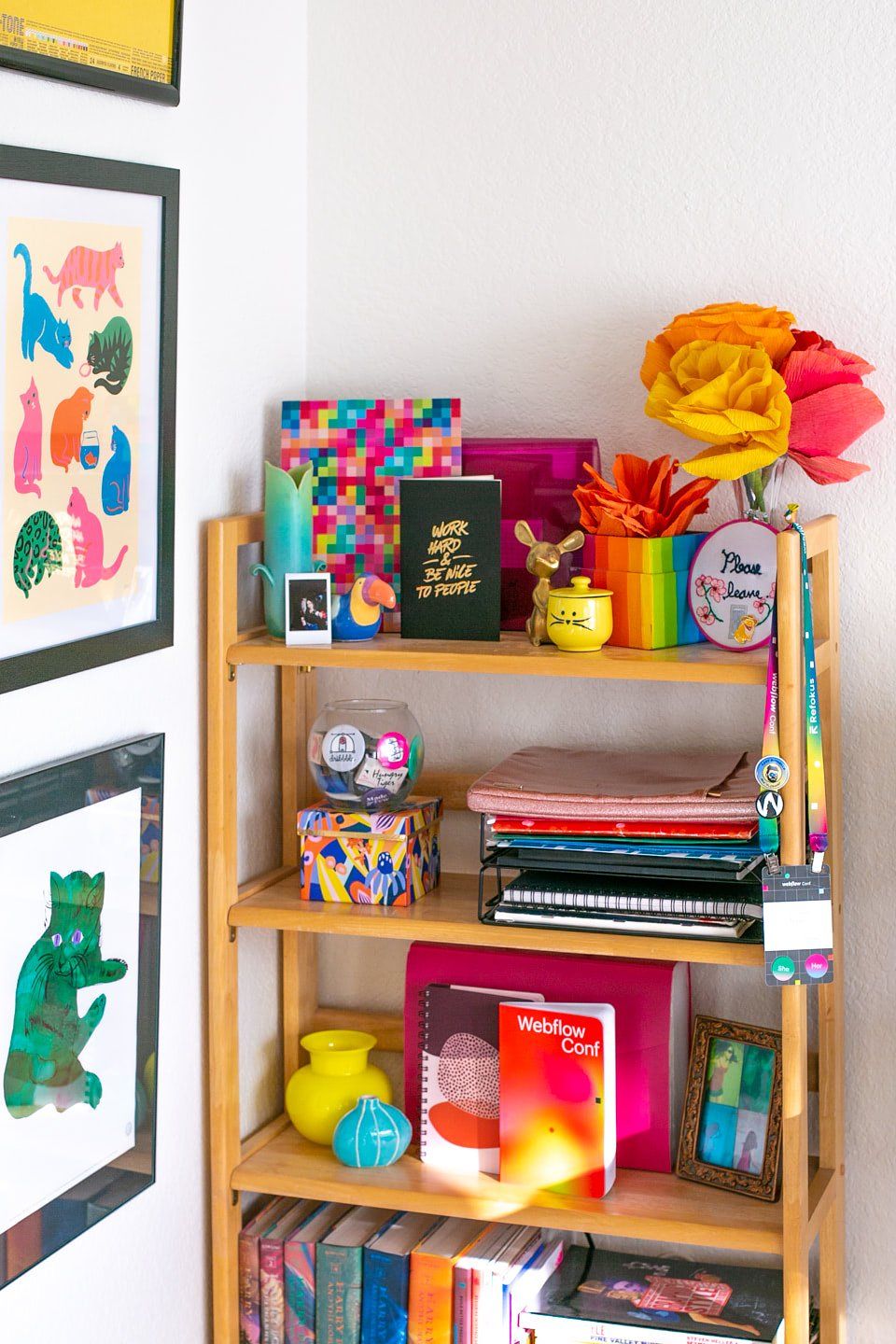 A freestanding ladder bookshelf with fiction books, colourful vases, photos, and notebooks