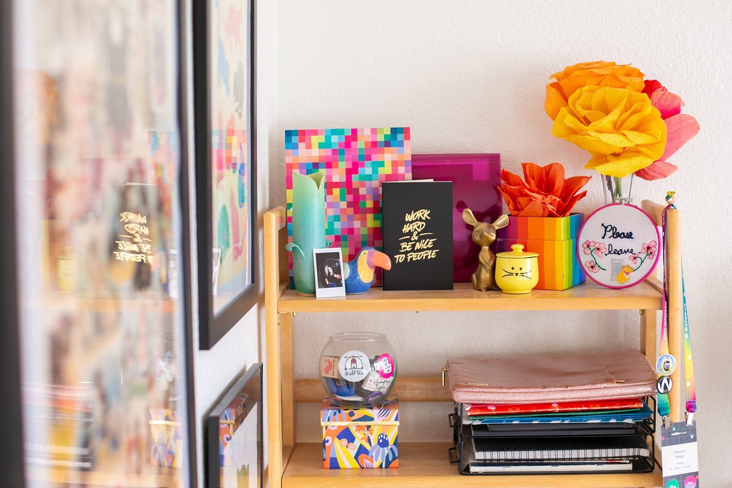 A view of the top part of a ladder bookshelf in a home office, adorned with colourful notebooks, postcards, paper flowers, candles, figurines, and photographs