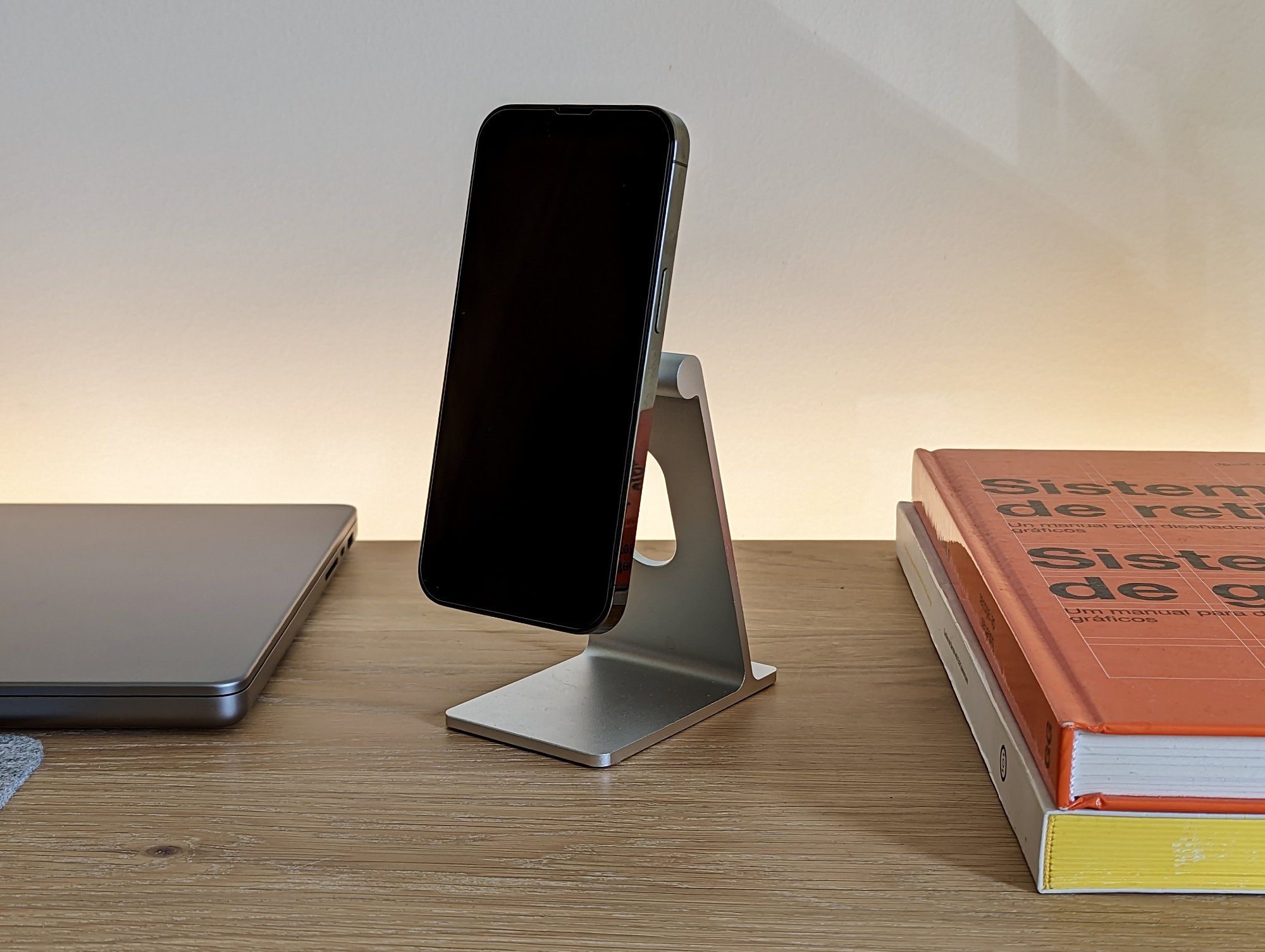 A phone stand with an iPhone on it, a MacBook, and a couple of design books on the desk