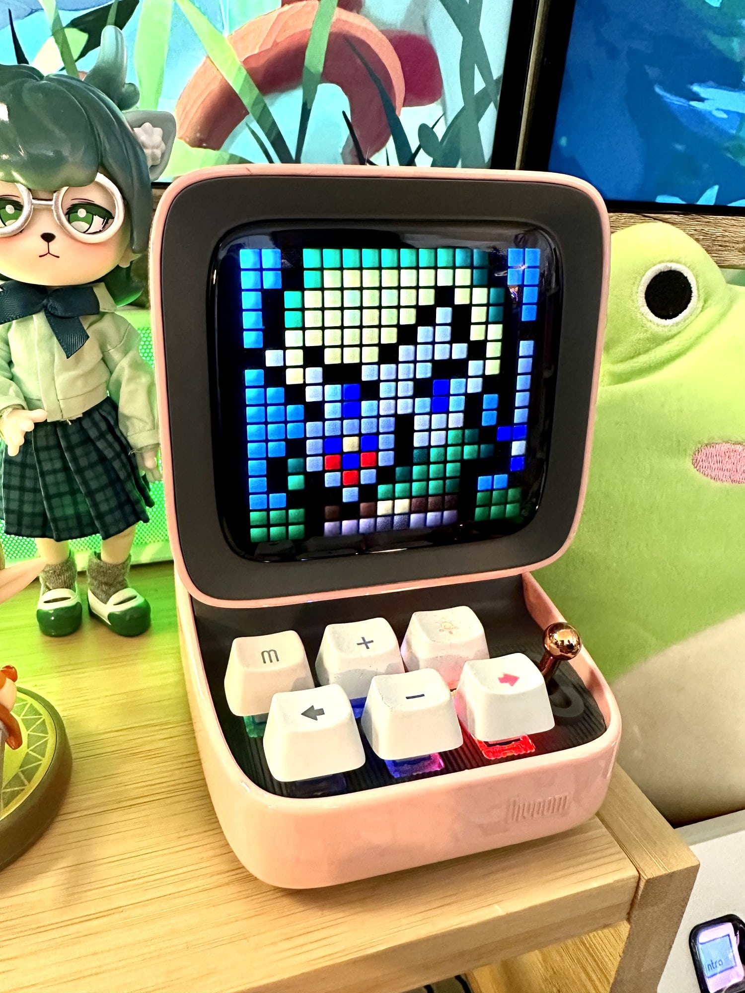 A Divoom Ditoo Pixel Art portable speaker in pink with a Penny’s Box doll behind it