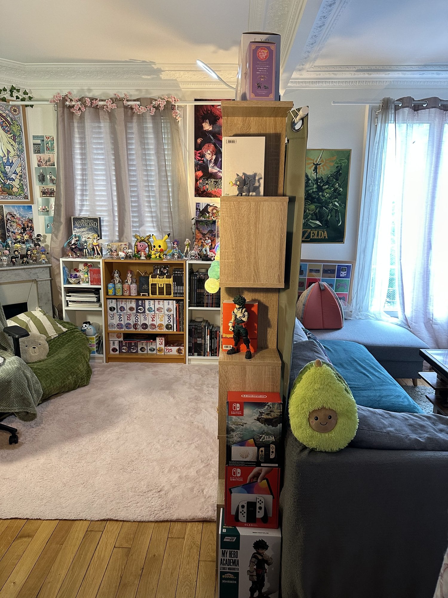 A living room featuring Japanese soft toys, video game wall art, and manga & anime figurines is divided into two sections by bookcases