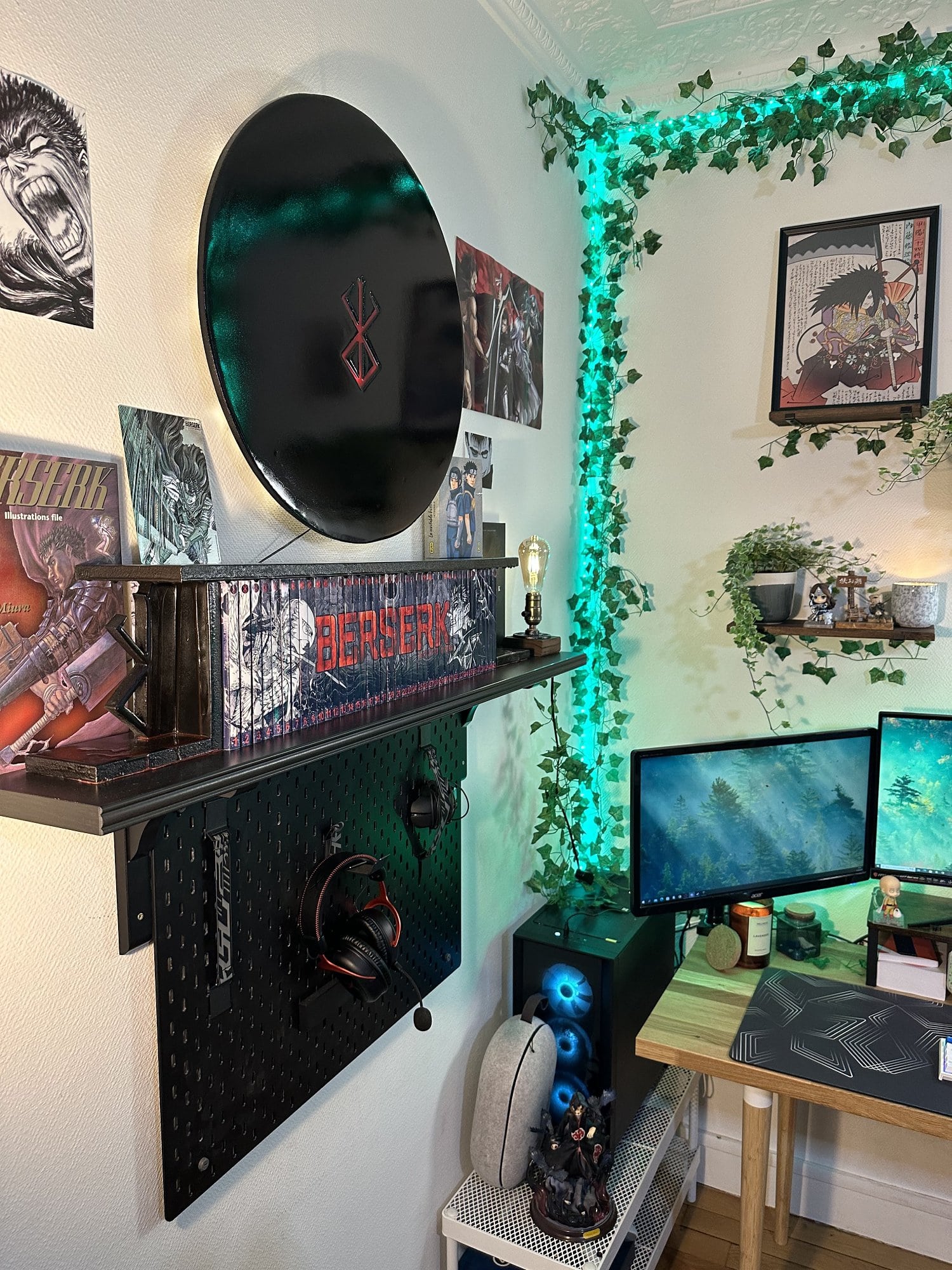 A personal home battlestation featuring two gaming monitors, fake climbing ivy, a black pegboard holding headphones and a mouse, and a Berserk anime silhouette light on the wall