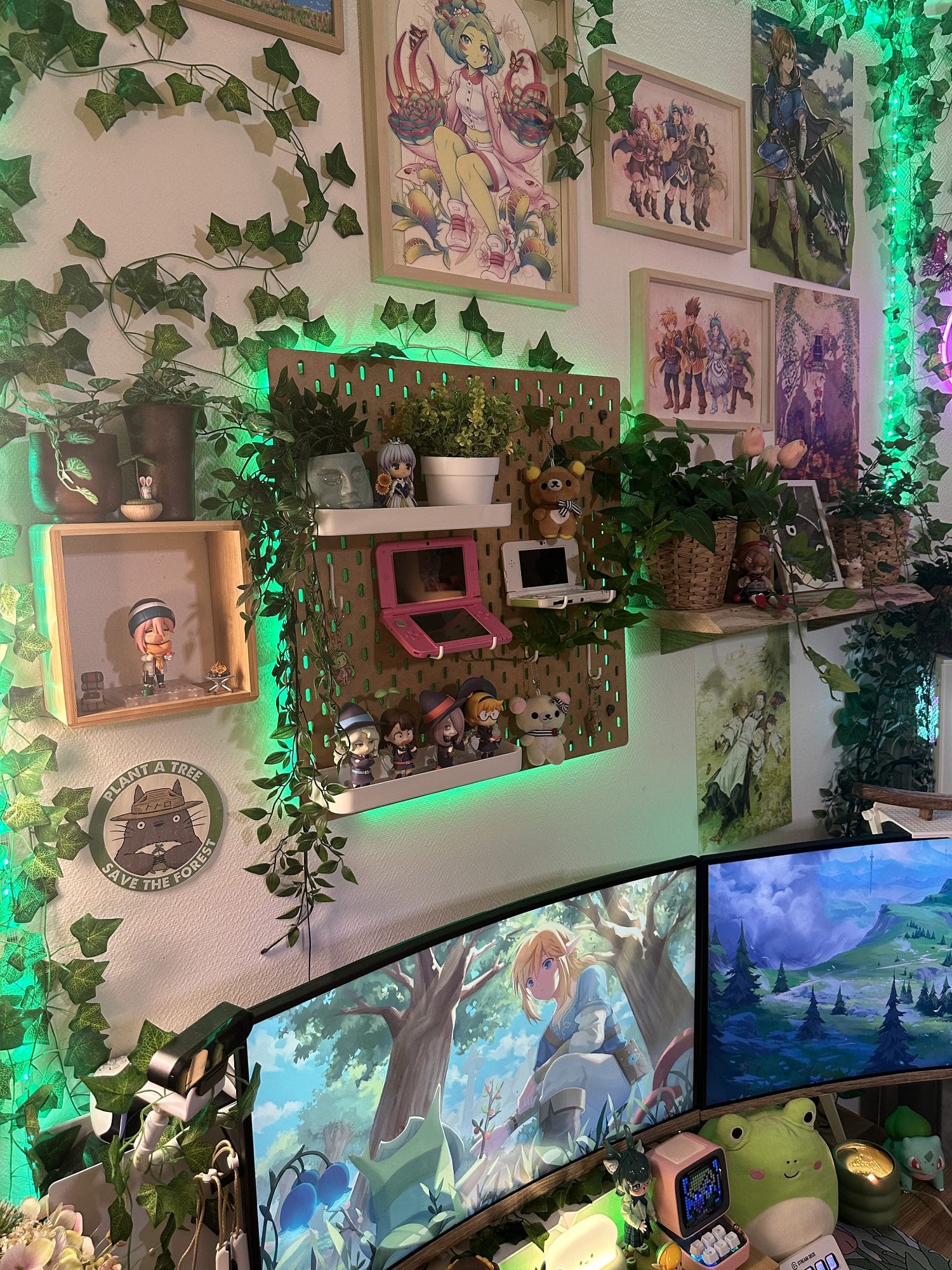 A cosy anime- and Zelda-inspired multiple screen battlestation with lots of figurines, artificial plants, and wall art