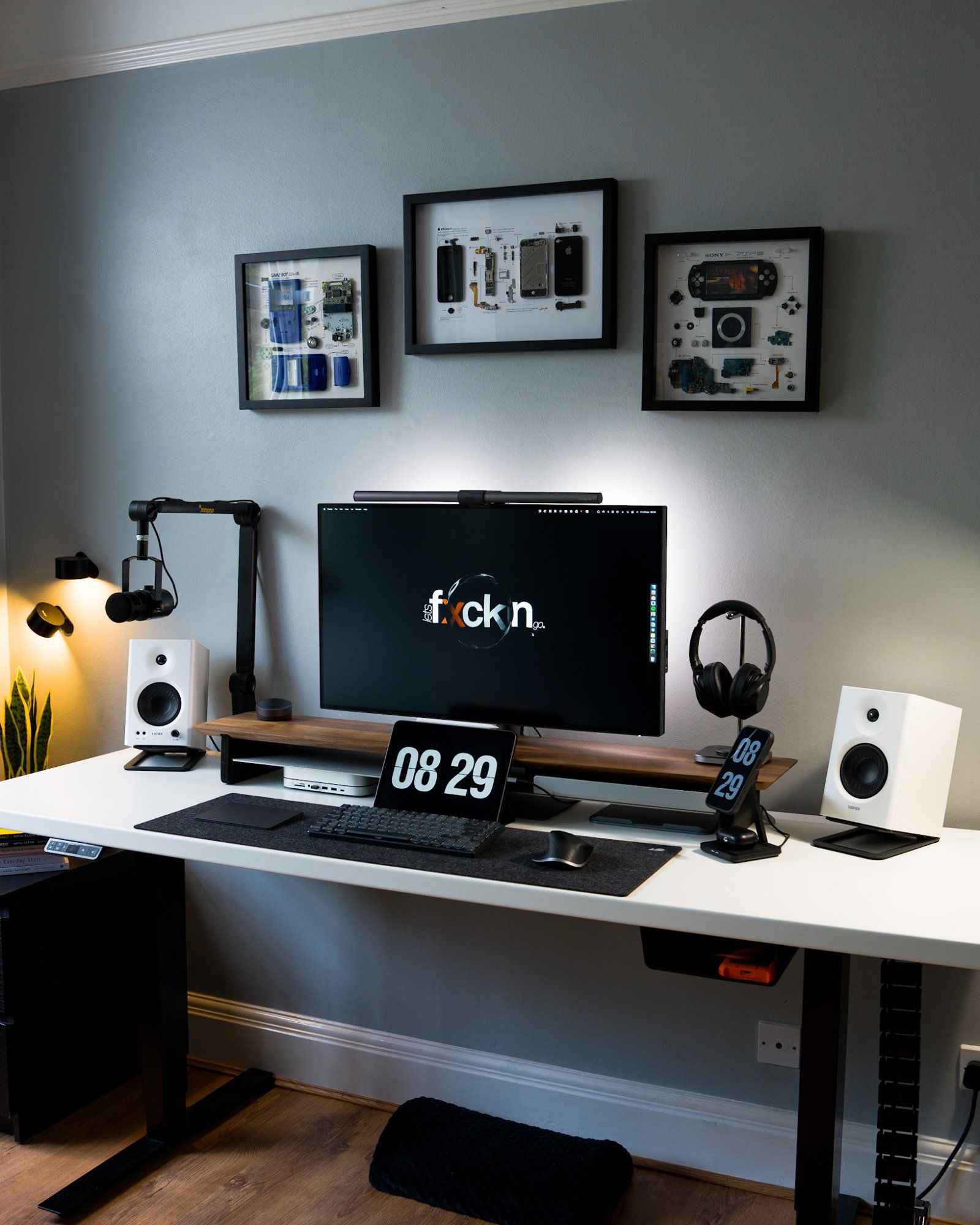 A minimal Friska standing desk setup with framed wall art featuring three disassembled devices