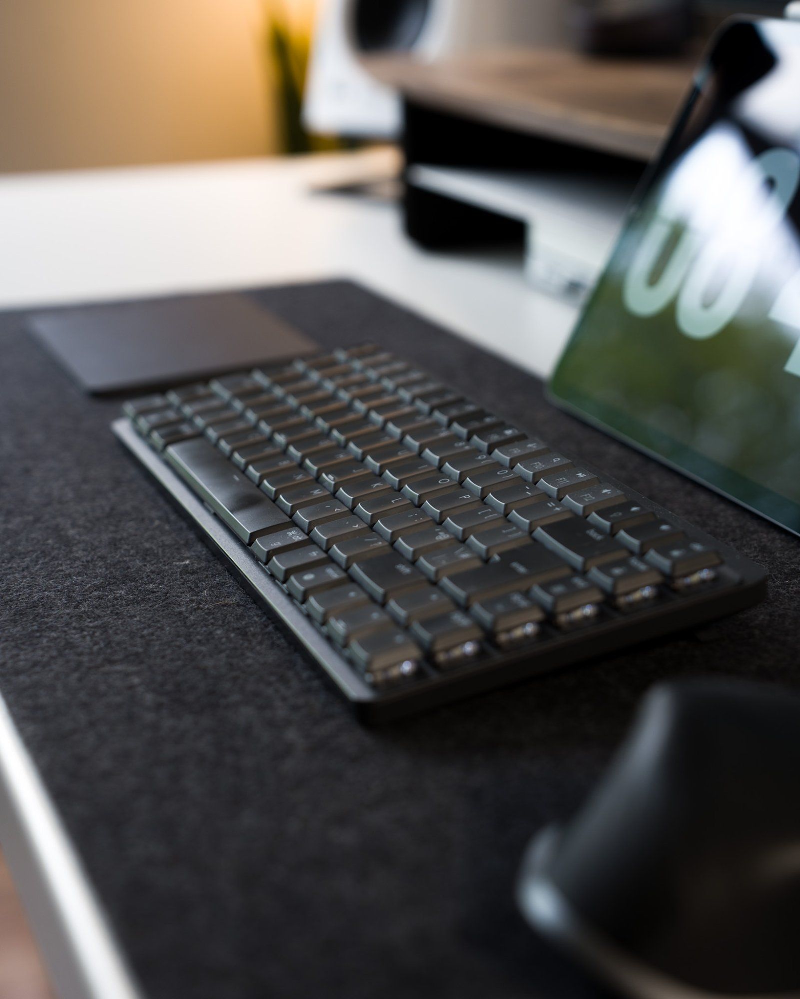 A side view of a mechanical keyboard, a mouse, and a trackpad lying on a wool desk mat