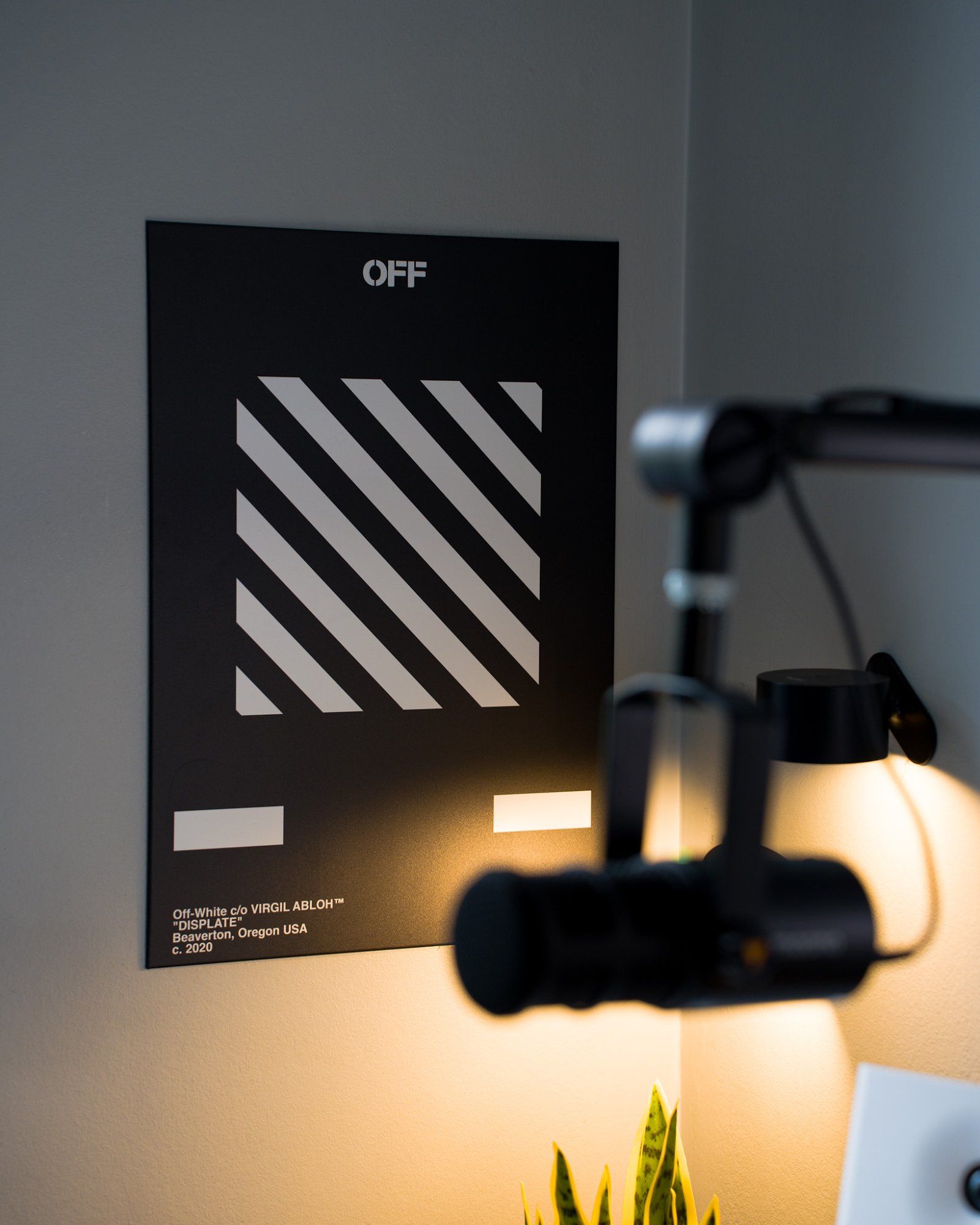 An Off White DISPLATE Stripes poster by American fashion designer Virgil Abloh hanging on the wall in the background in focus; towards the foreground is an out-of-focus Maono PD400X microphone