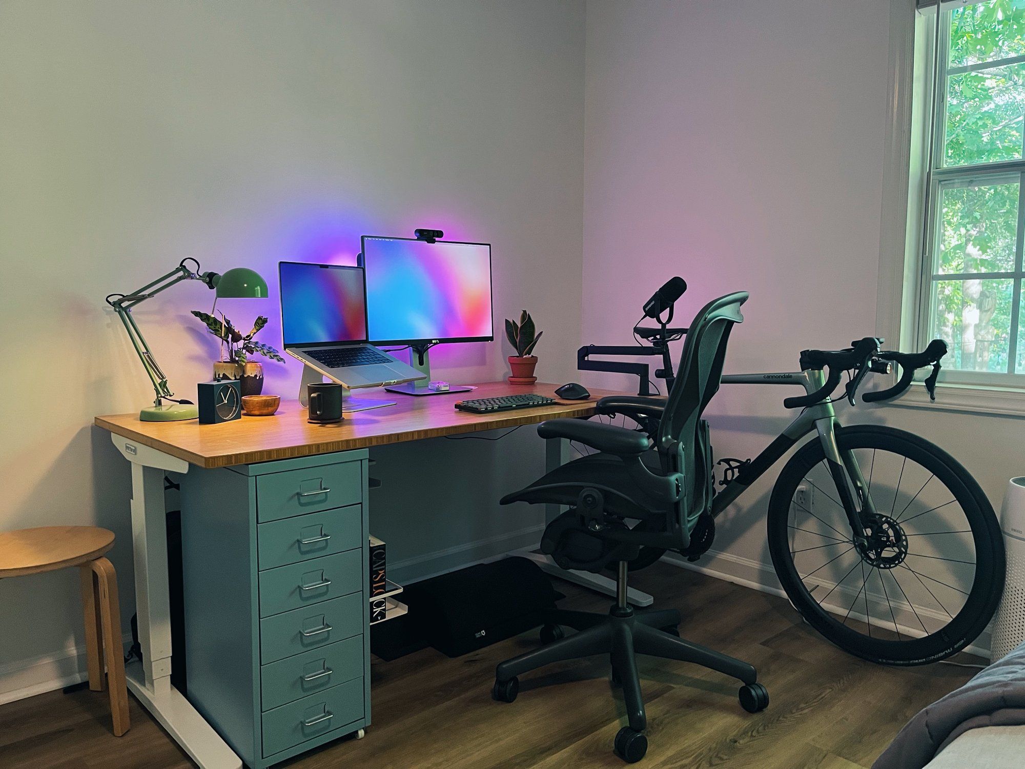 A minimalist and well-organised designer’s home office featuring an Uplift V2 standing desk, a Herman Miller Aeron chair, and a bicycle positioned near the window
