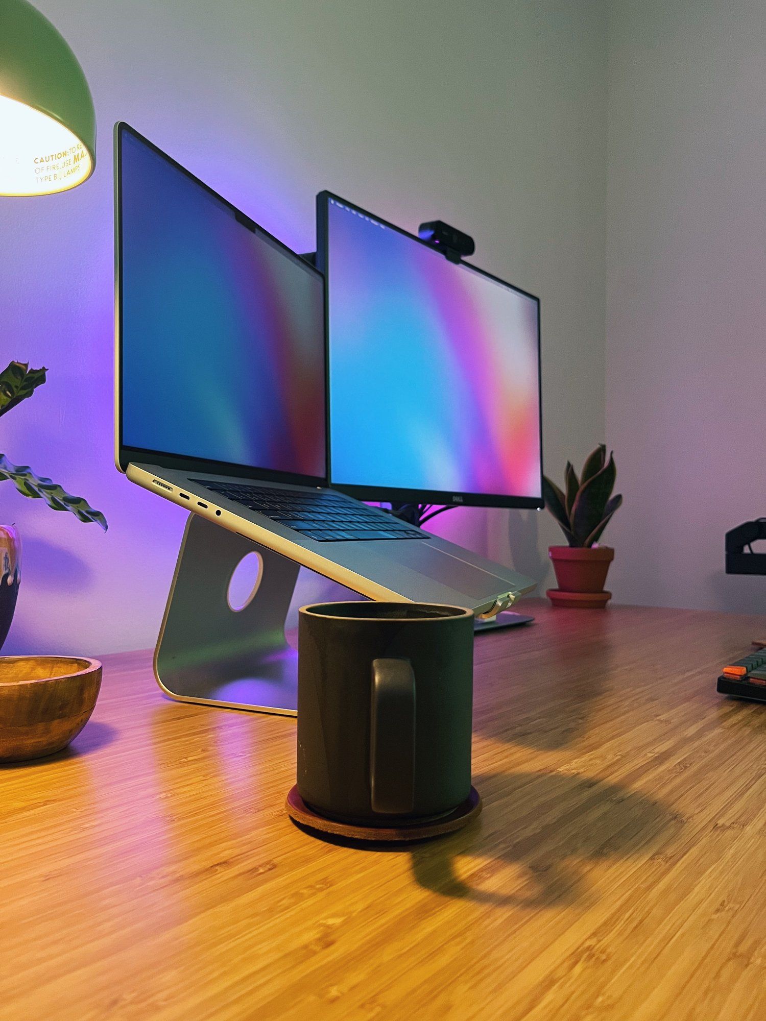 A desk setup shot from the left side with a mug in the foreground and a laptop, a monitor and a houseplant in the background