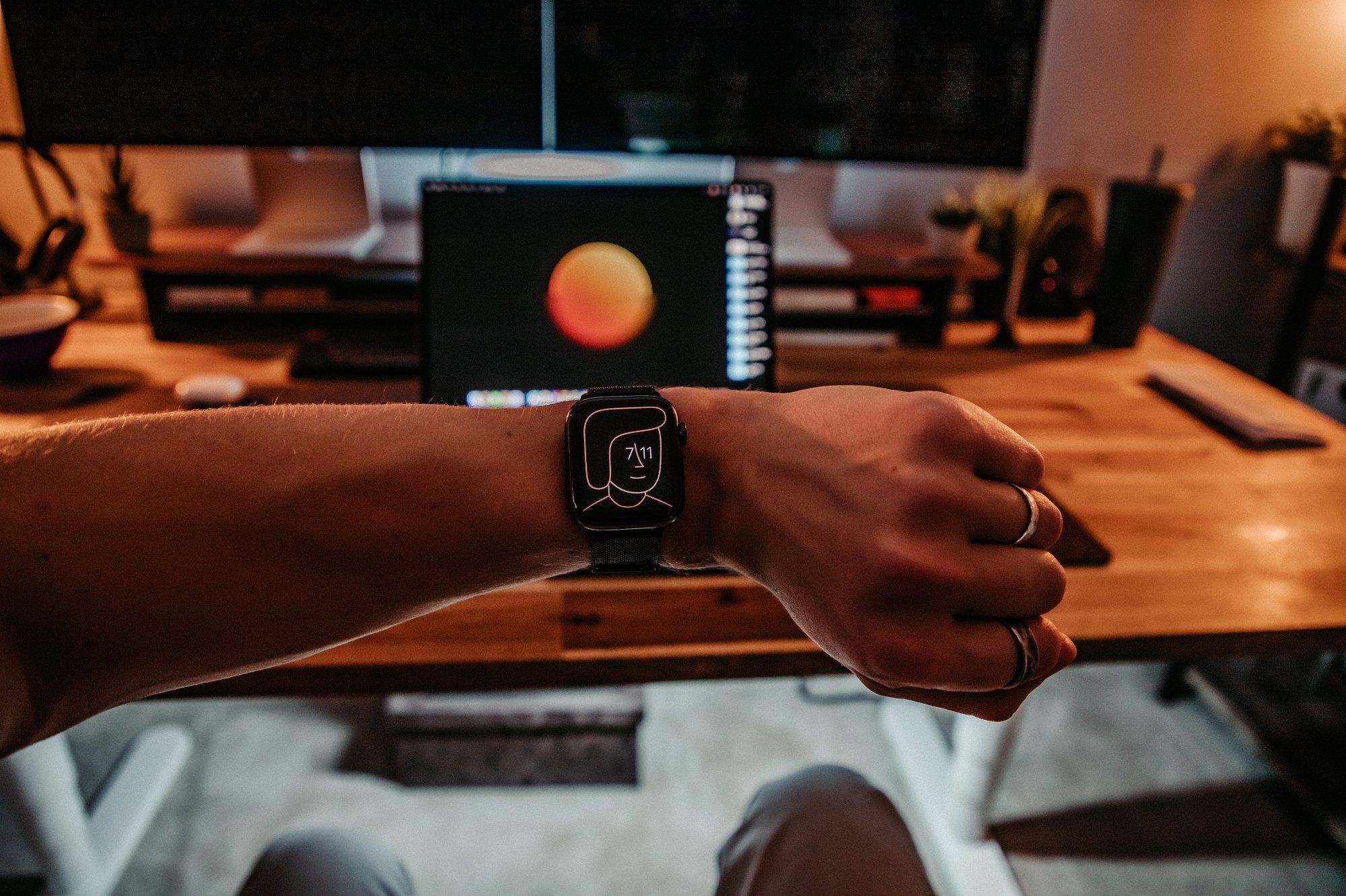 A man’s hand with a wristwatch is in the foreground, and a MacBook Pro is in the background