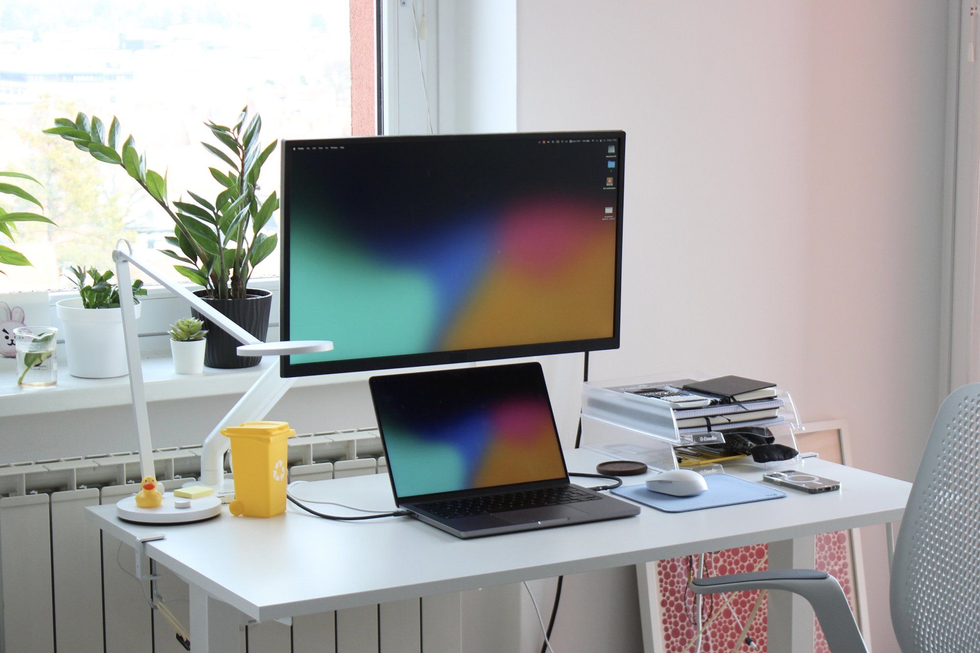 A well-organised sit-stand desk setup by the window with plants on the windowsill