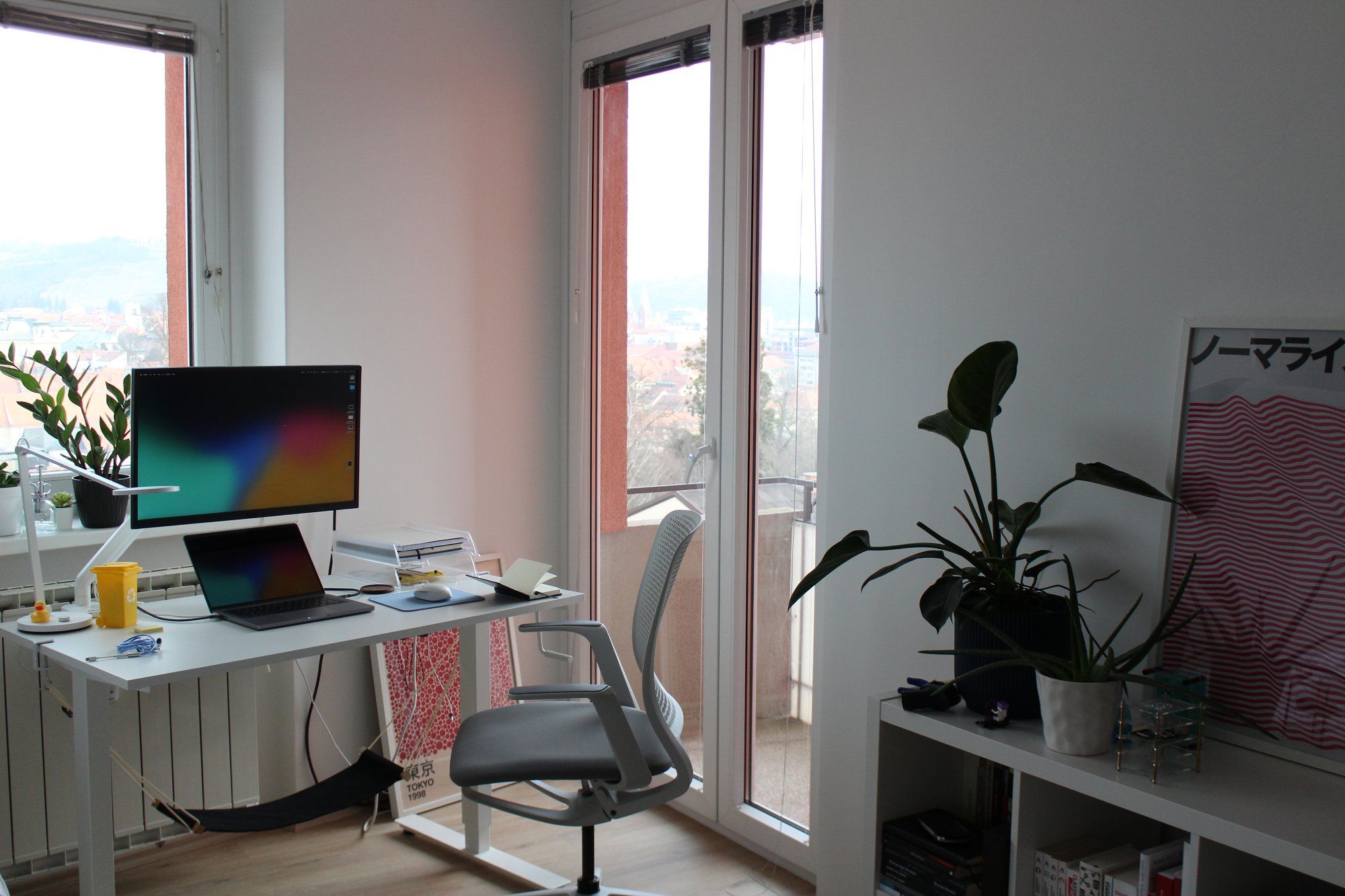 An IKEA standing desk with a footrest hammock in front of the window and next to the balcony door