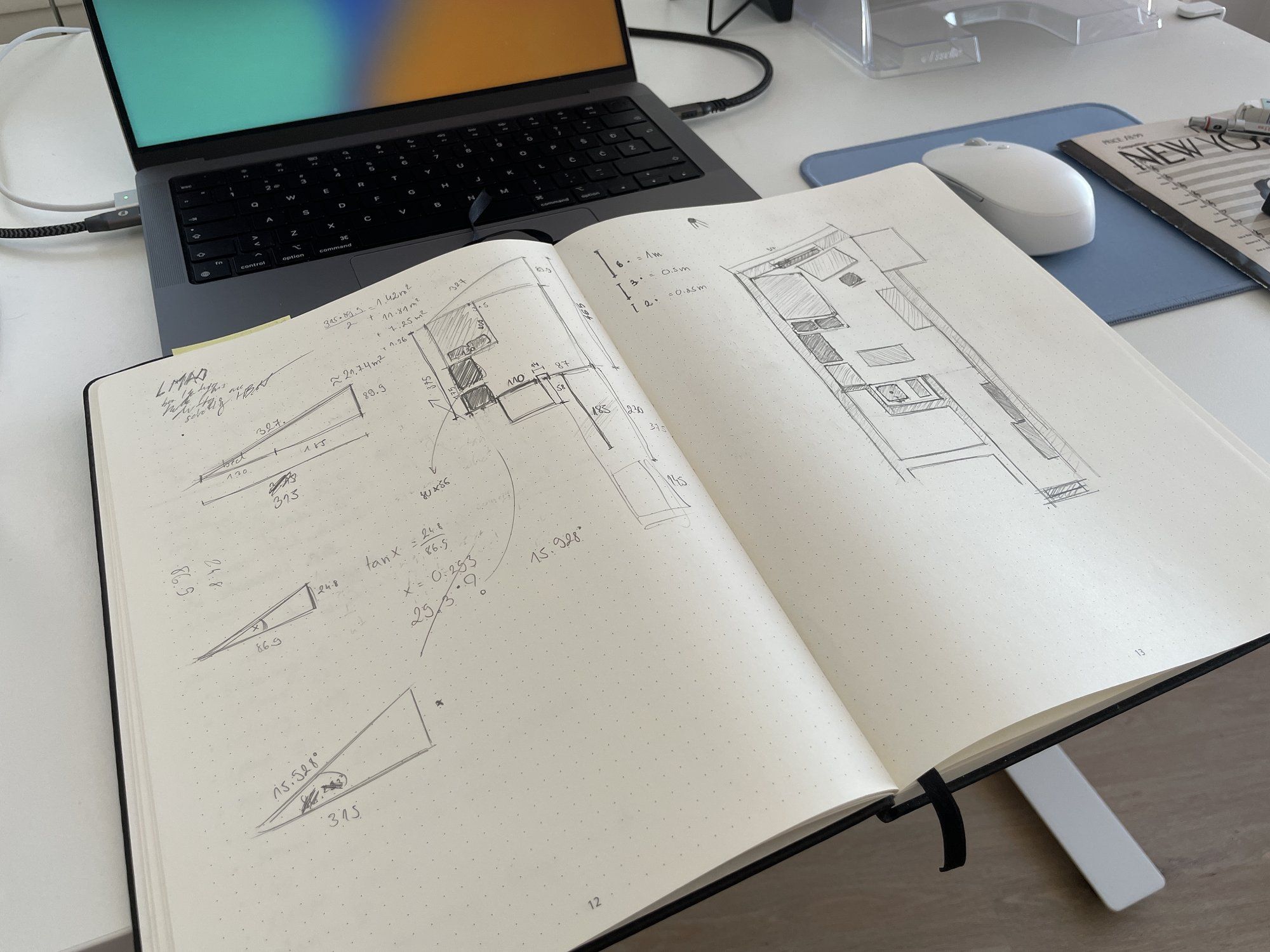 A notepad with blueprints, calculations, and sketches lies in front of the MacBook Pro on the desk