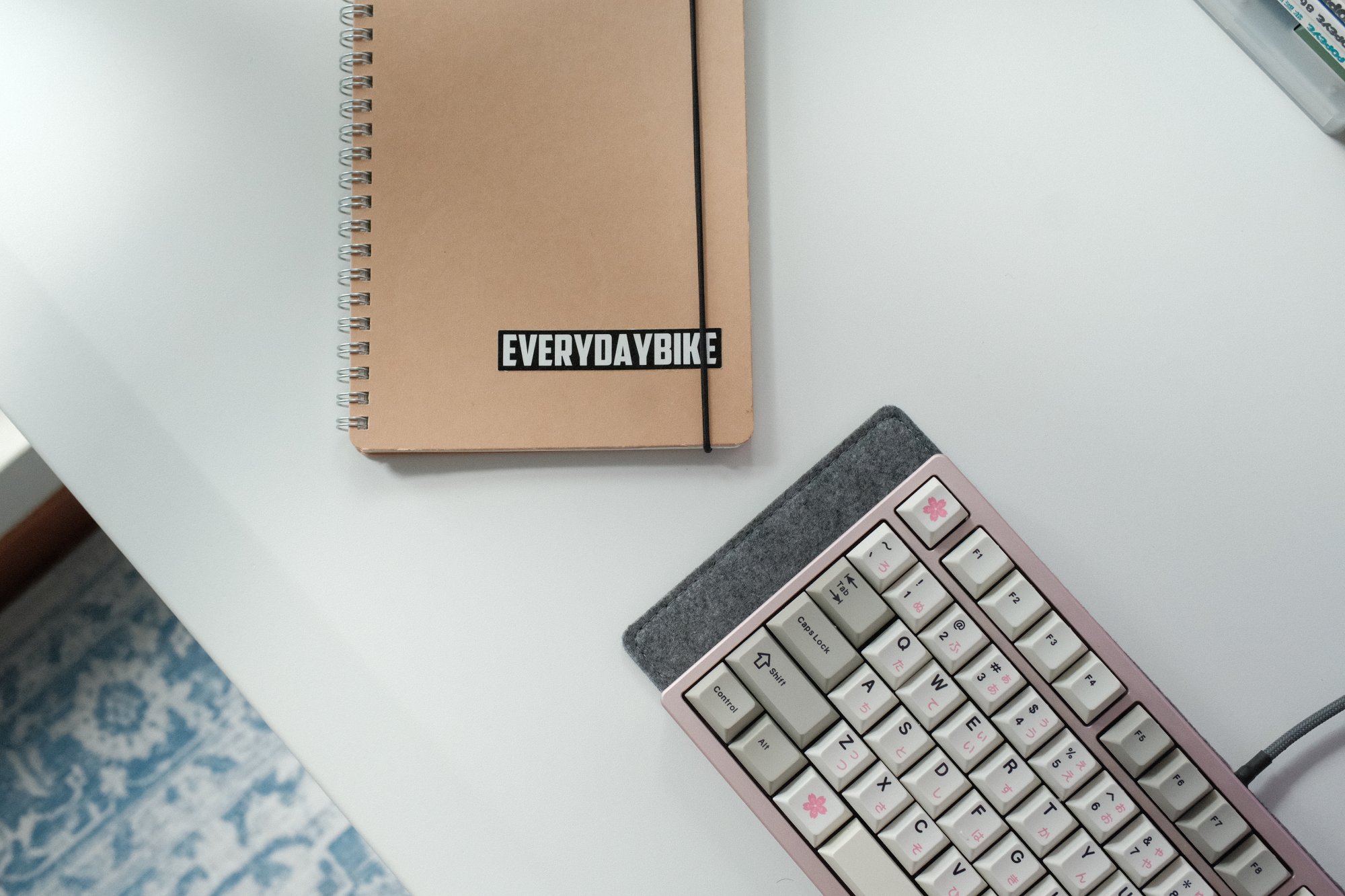 An EVERYDAYBIKE notepad and a pink custom mechanical keyboard lying on a white desk