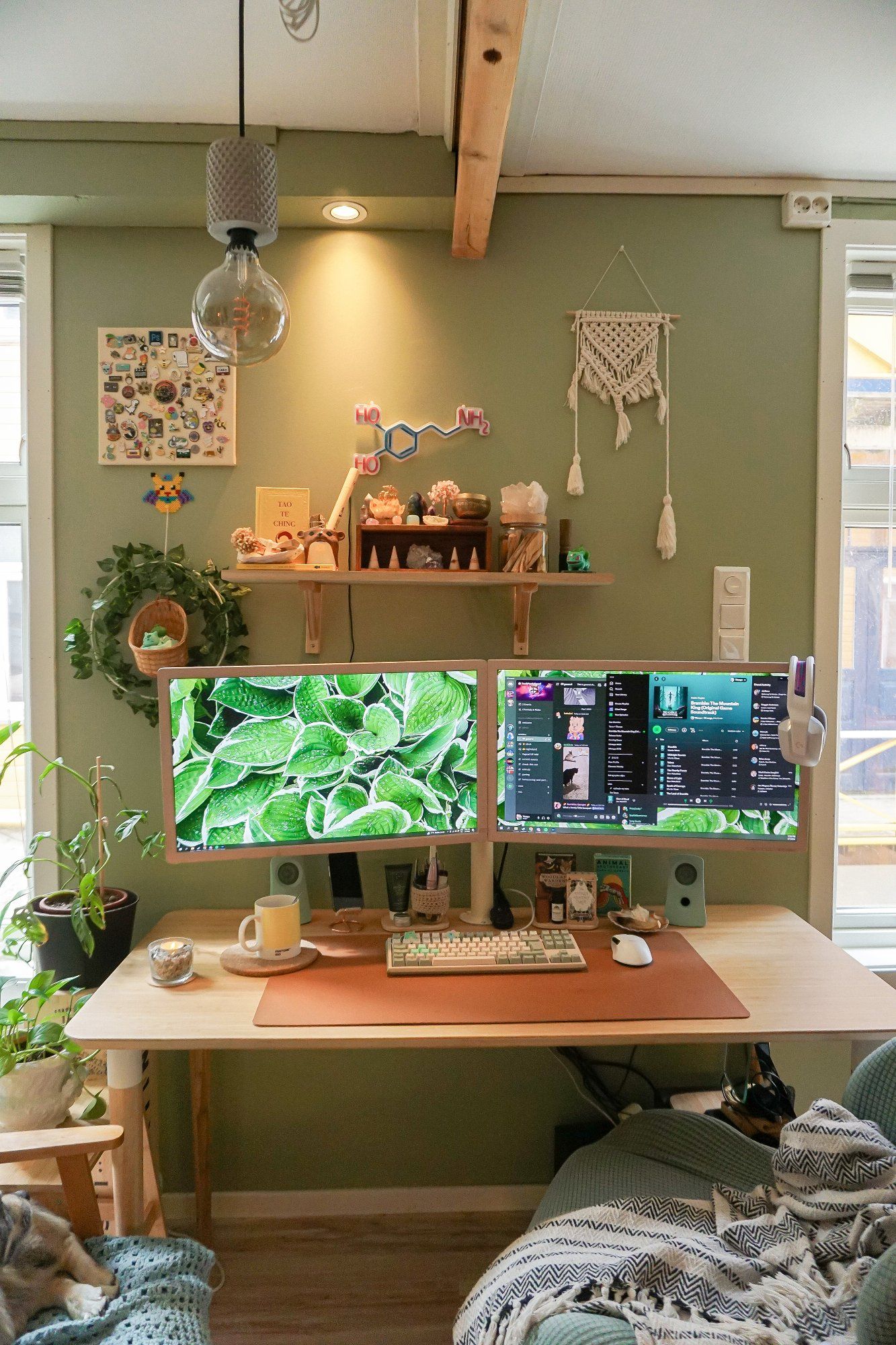 A dual-monitor home office with a macramé wall-hanging, a Dopamine neon light, a pin collection, and many other cute dècor items