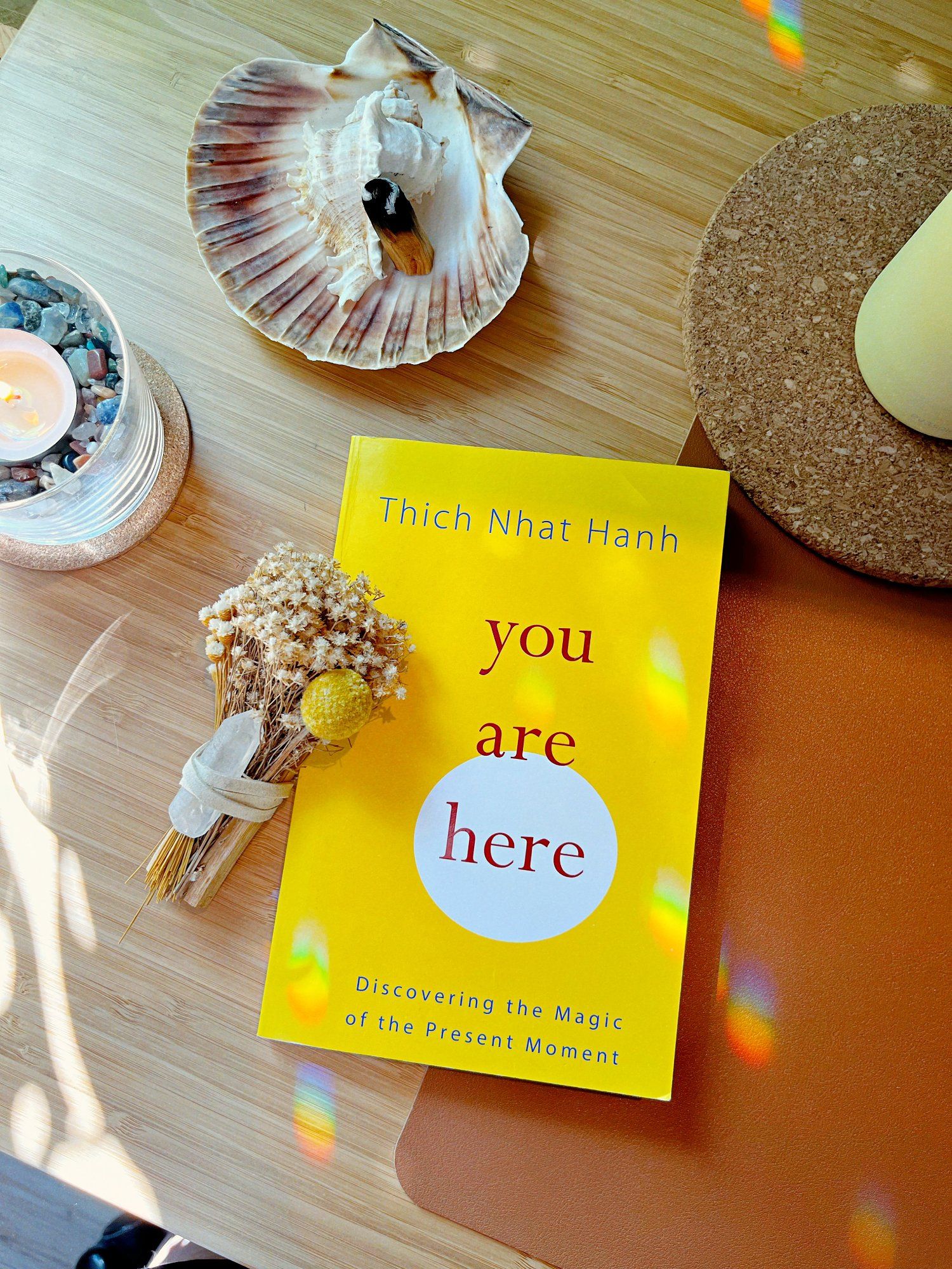 a book called You are Here by Thich Nhat Hann on the table, along with dried flowers, a candle, and a seashell