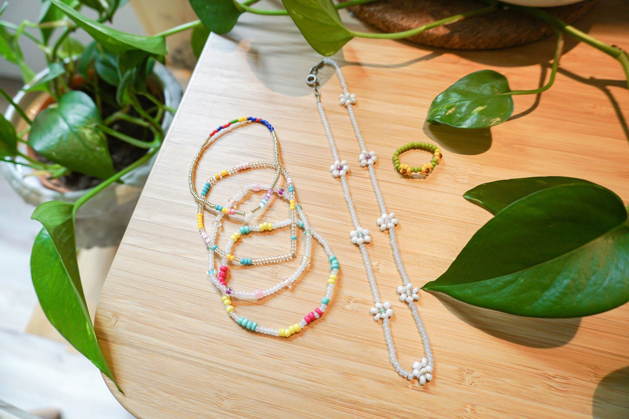 Beaded necklace and bracelets lying on the desk, surrounded by green leaves of indoor plants