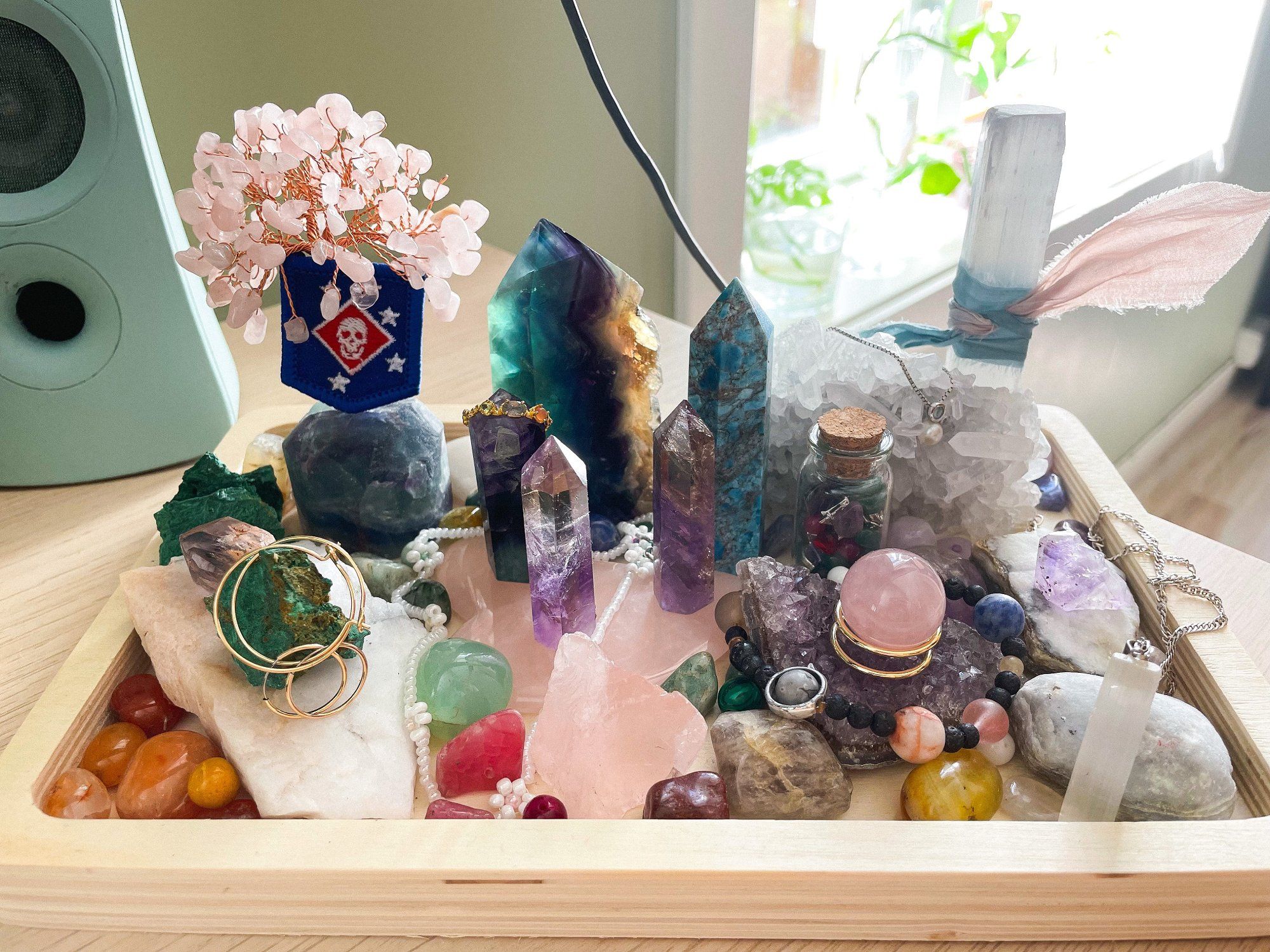 A wooden tray holds a collection of crystals, stones, and jewellery