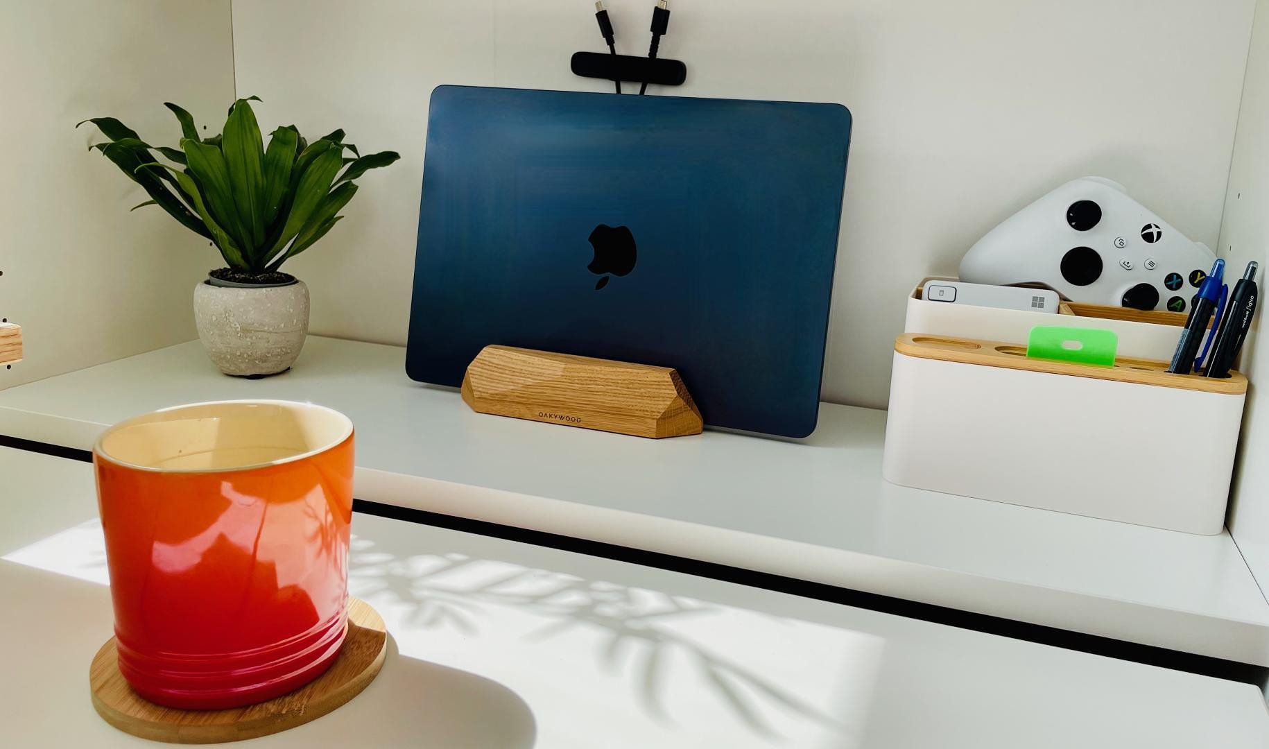 A corner of a Scandinavian workspace featuring a shelf with a MacBook on a stand, a small houseplant, and some stationery