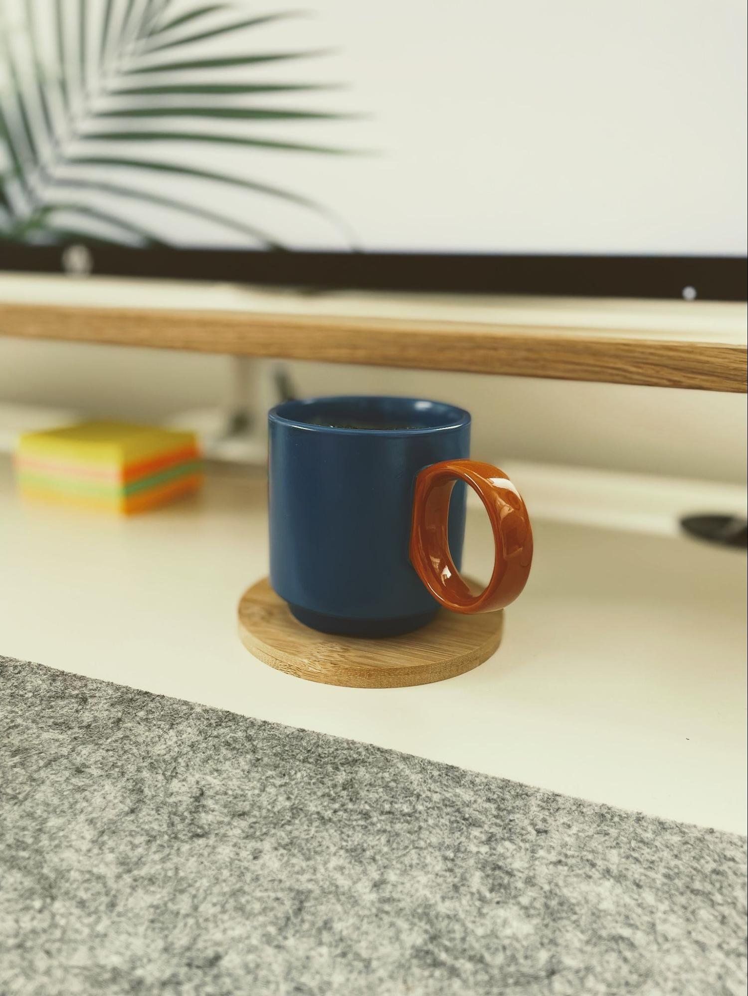 A cup of coffee sitting on a wooden coaster on a desk