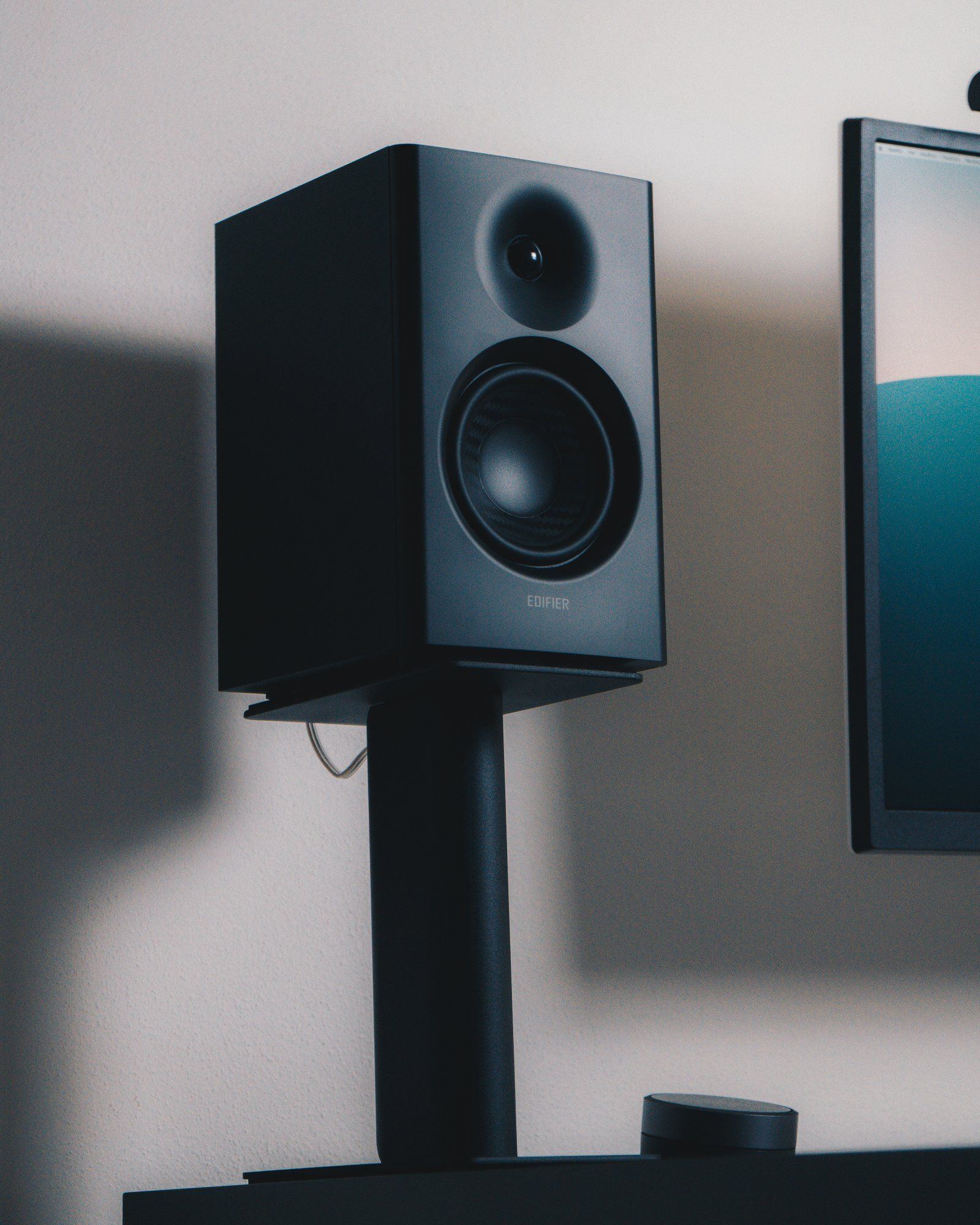 A close-up of a black Edifier speaker sitting on a Kanto stand