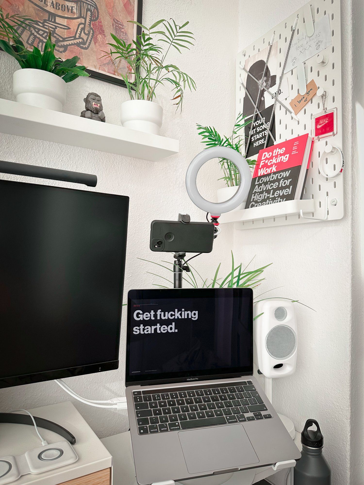 A corner of a small home office featuring a MacBook Pro and a white pegboard