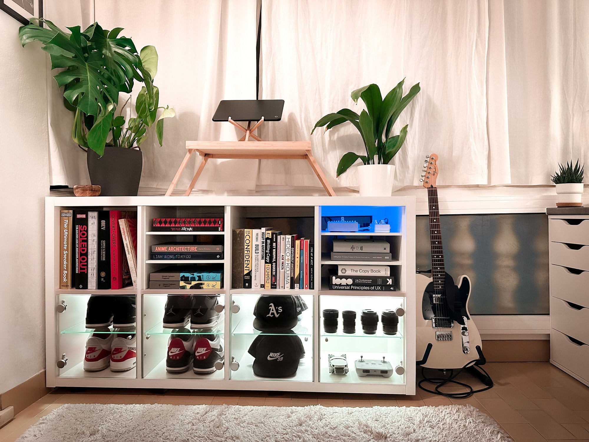 An IKEA KALLAX display cabinet filled with books, baseball caps, sneakers, and tech accessories