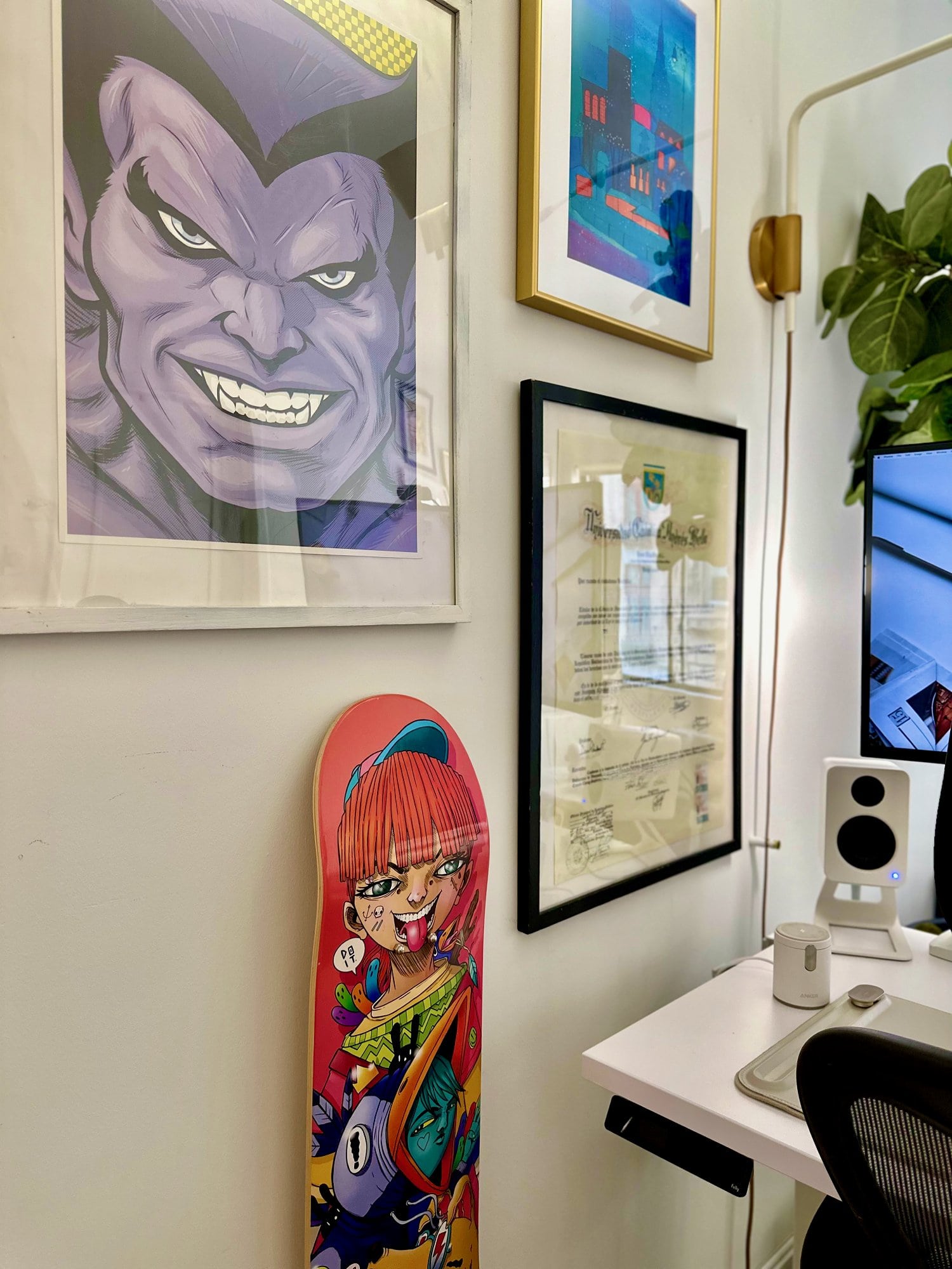 Three posters and a hand-painted skateboard on the wall in a home office