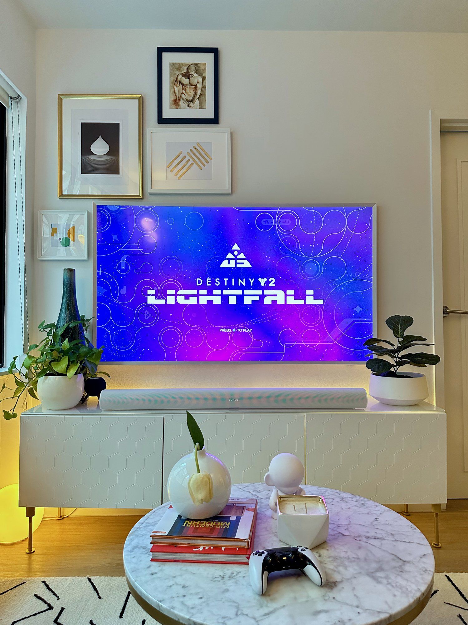 A large TV screen displaying the game Destiny 2: Lightfall for PS5, alongside a marble side table with some books, a vase, and a game controller