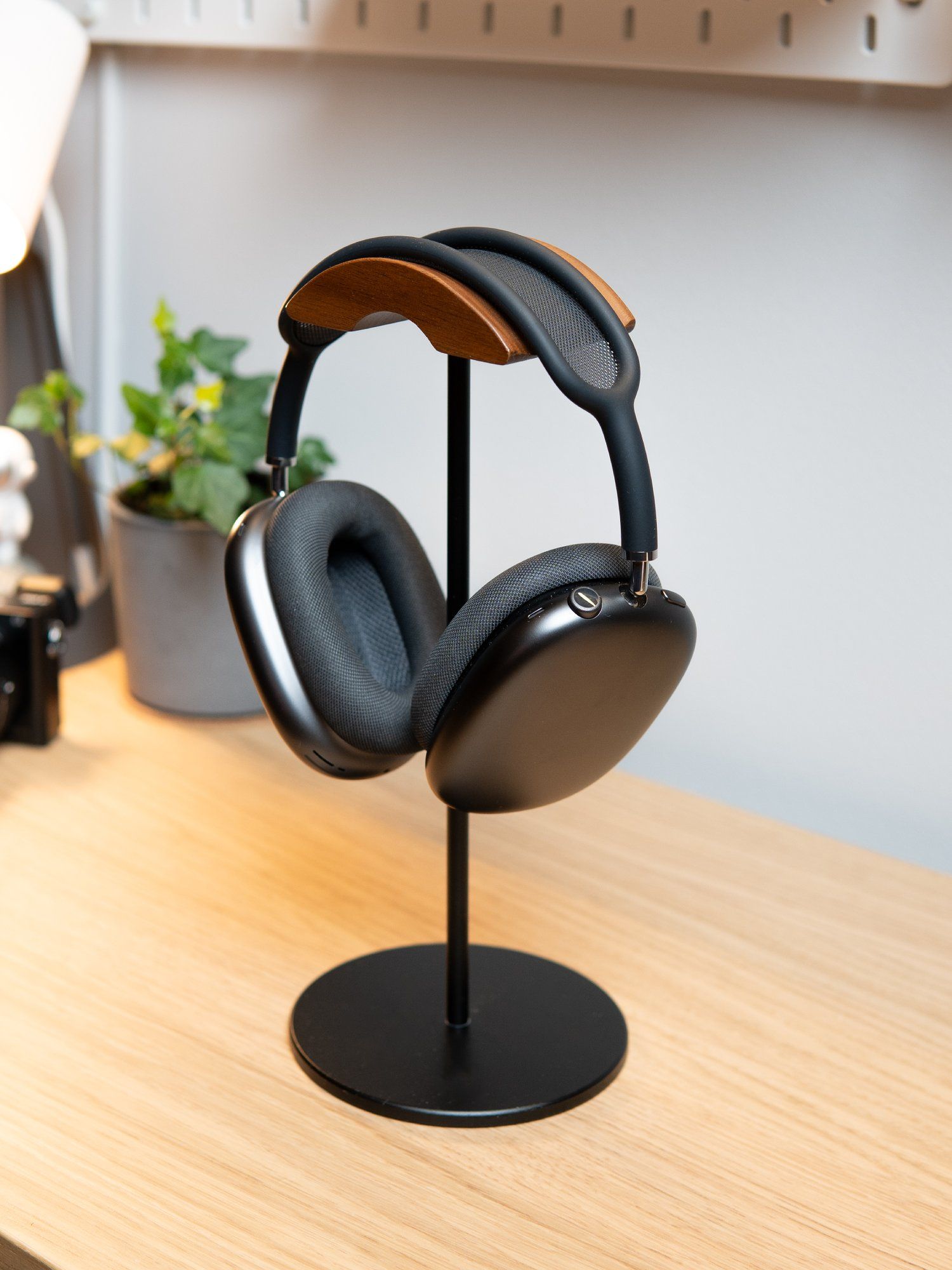 Apple AirPods Max resting on a stand, with a potted houseplant in the background