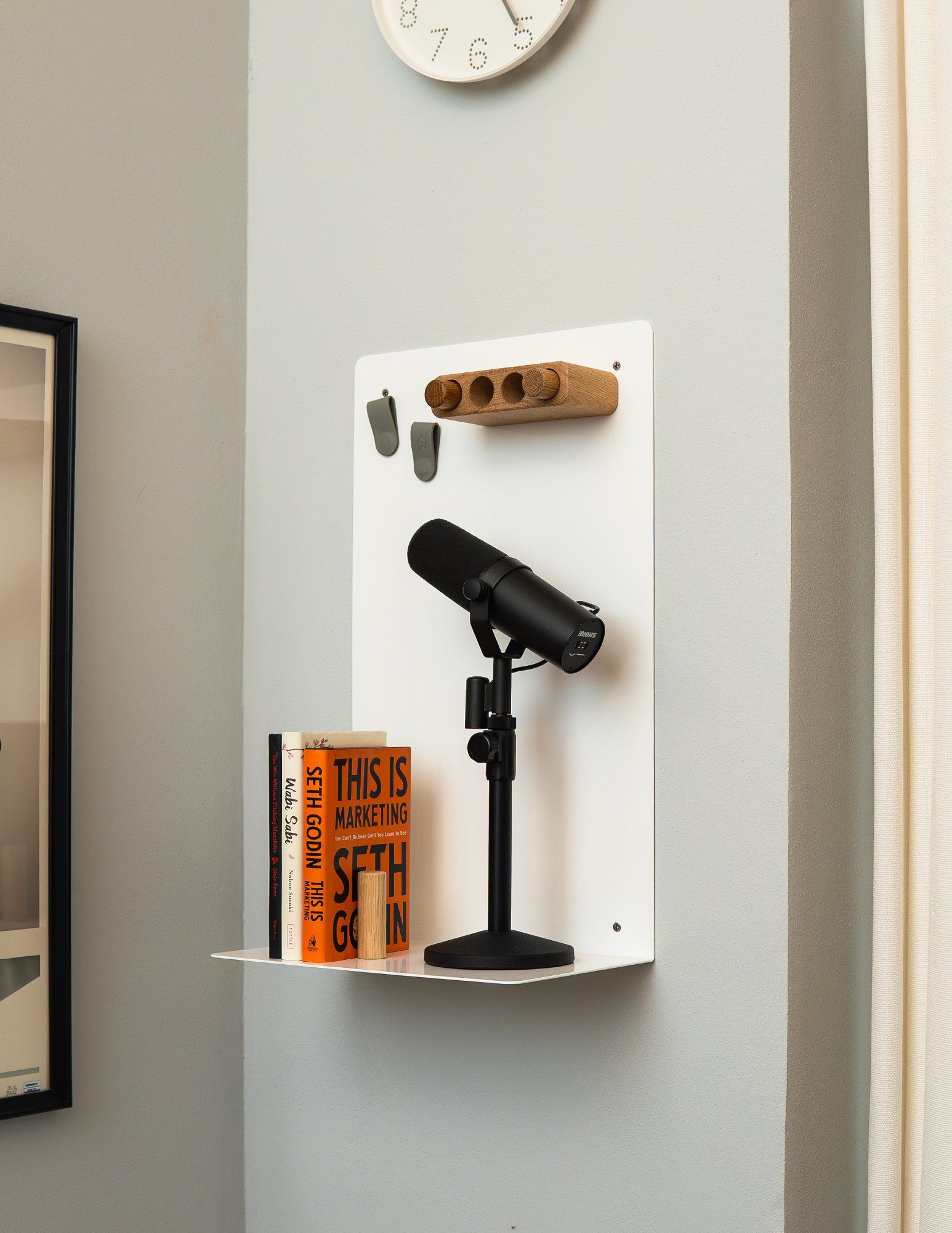 A Shure SM7B microphone and three books on a white minimalist wall shelf