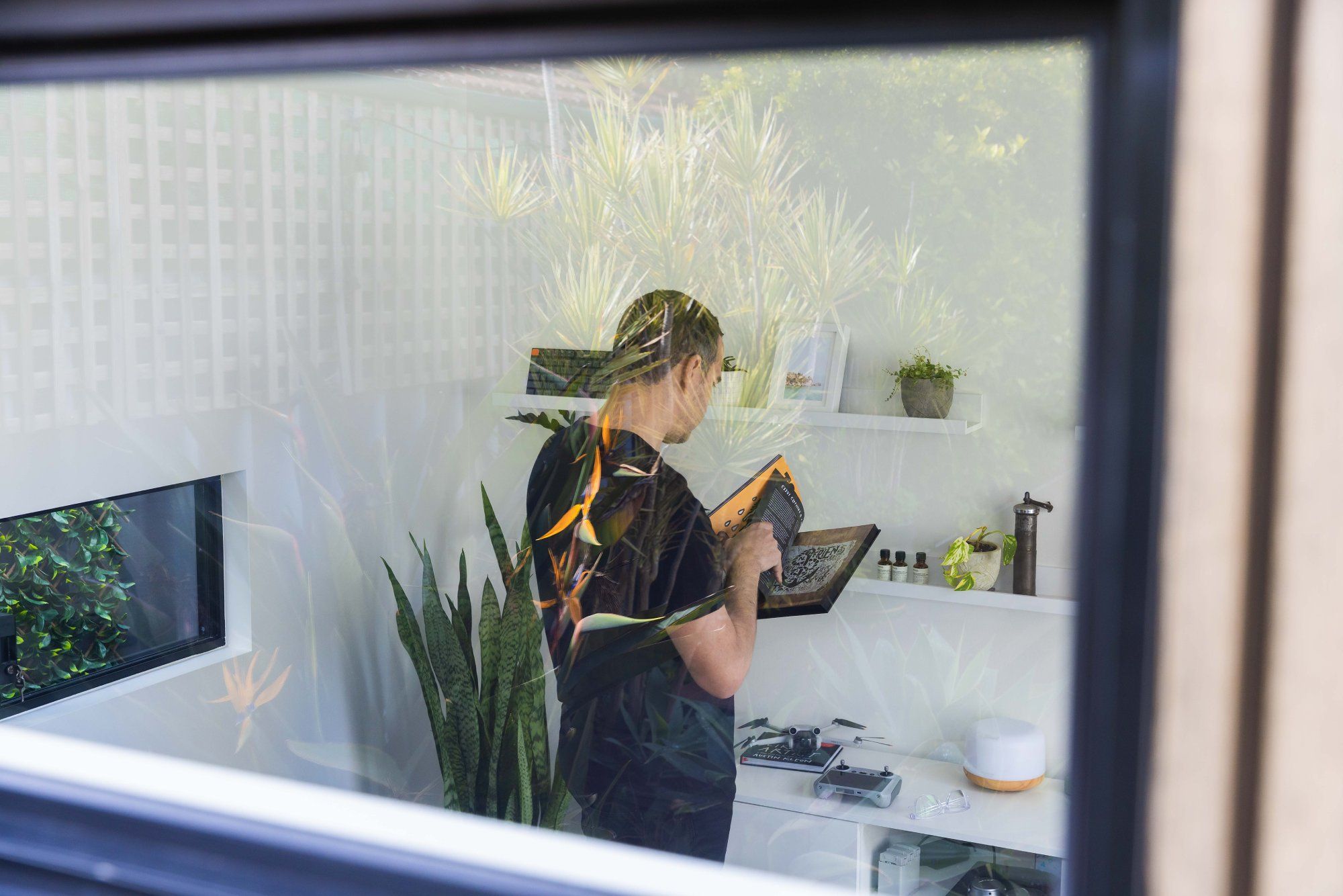 A photograph of Petar Ceklic in his home office, taken from behind through the window glass of his garden shed