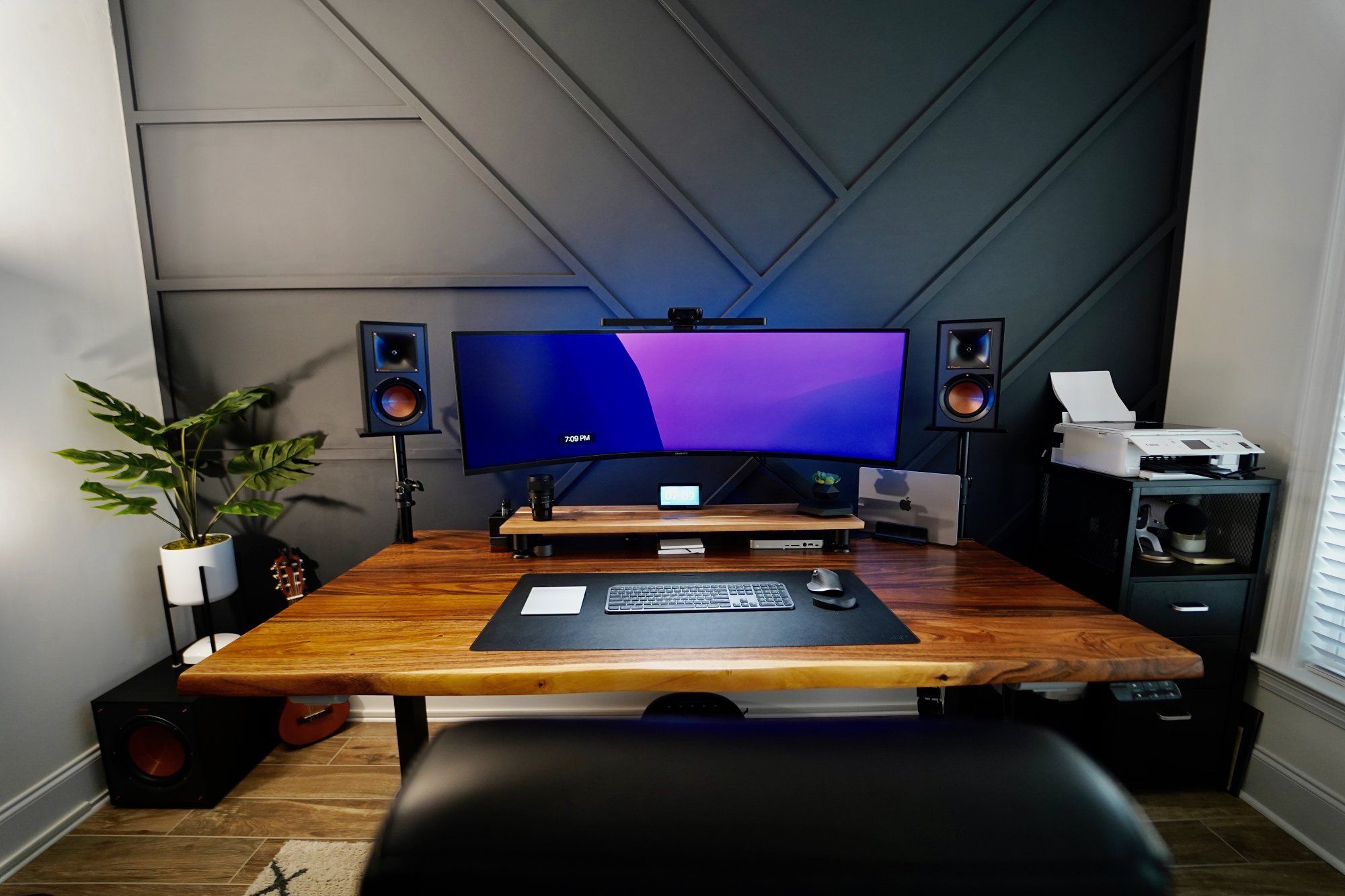 A spacious desk setup with a super ultrawide Samsung Odyssey monitor, Klipsch speakers, and a potted plant